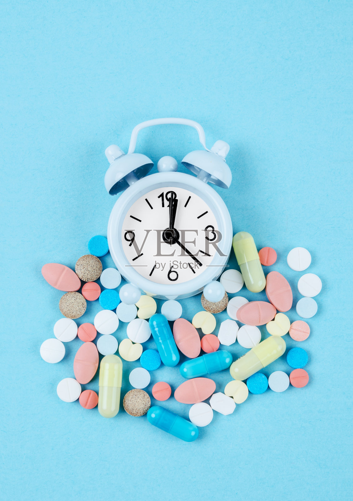 吃药的时间。高角度的彩色药物和药丸的闹钟在蓝色的背景。照片摄影图片