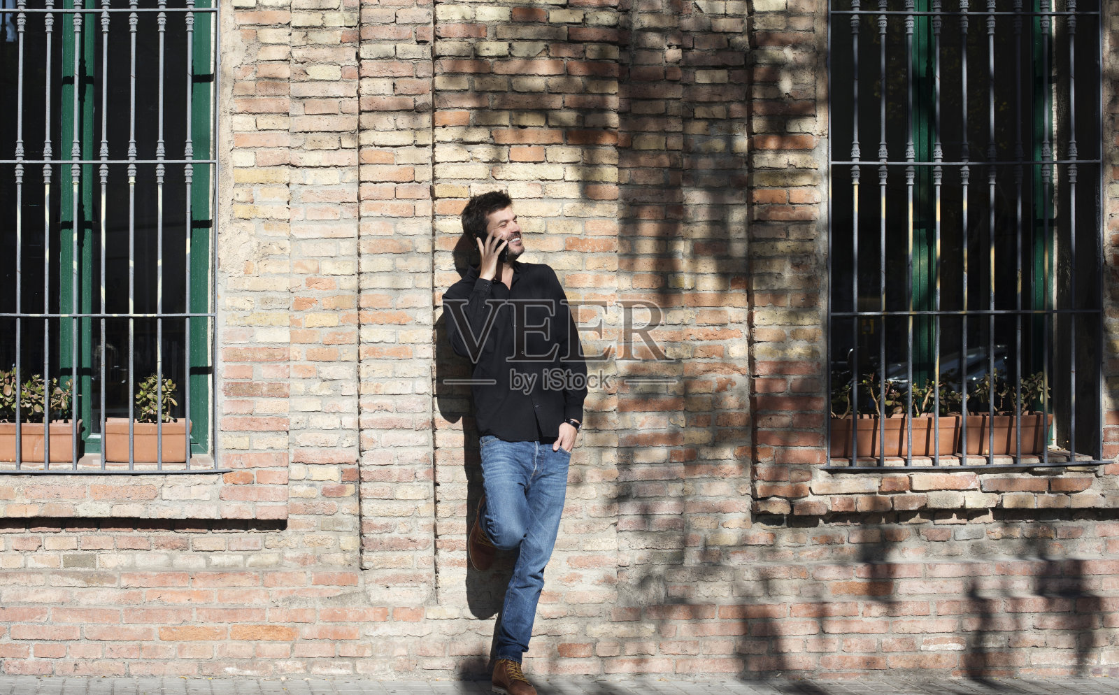 一个大胡子男人靠在墙上用手机聊天照片摄影图片