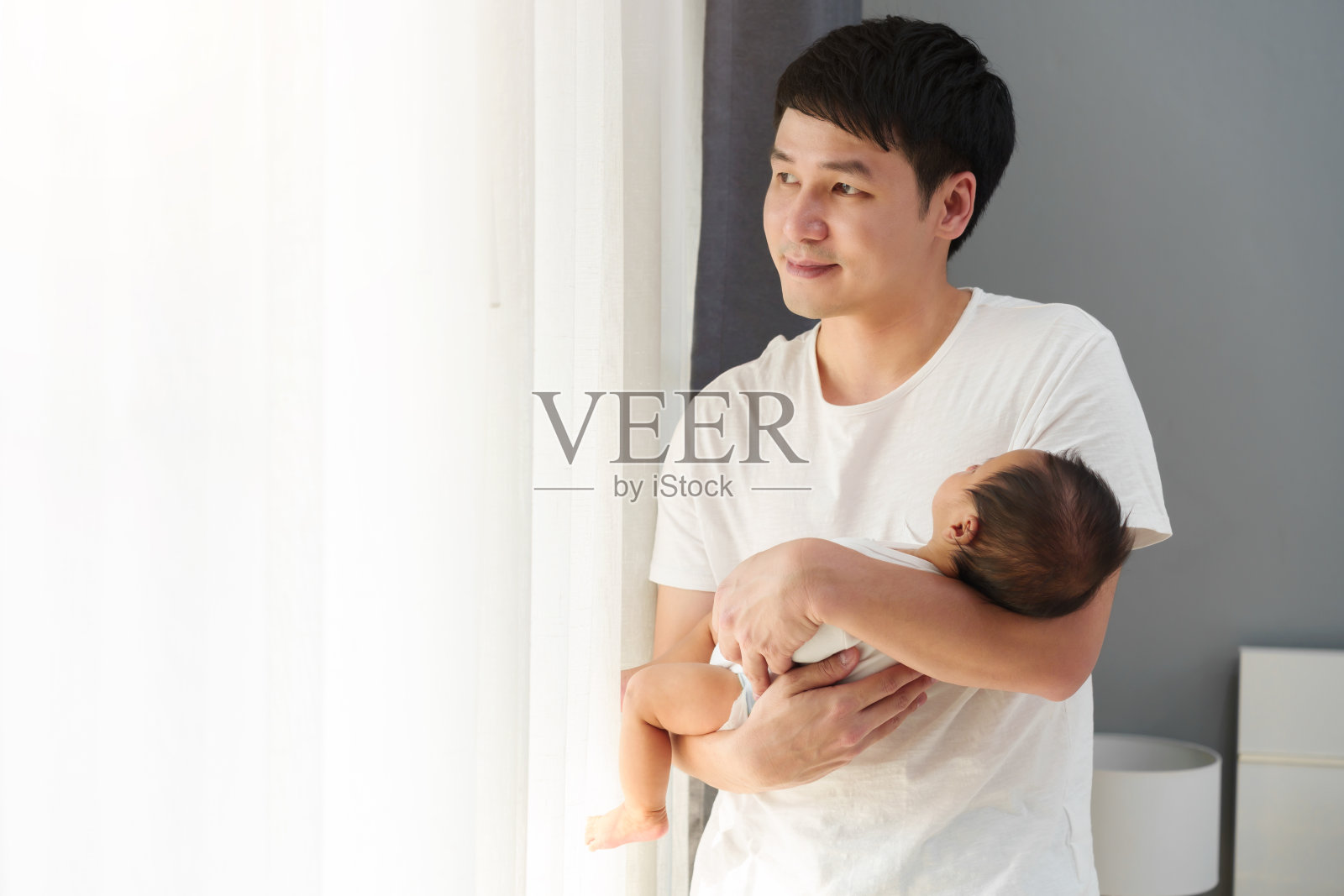 父亲抱着刚出生的婴儿望向窗外照片摄影图片