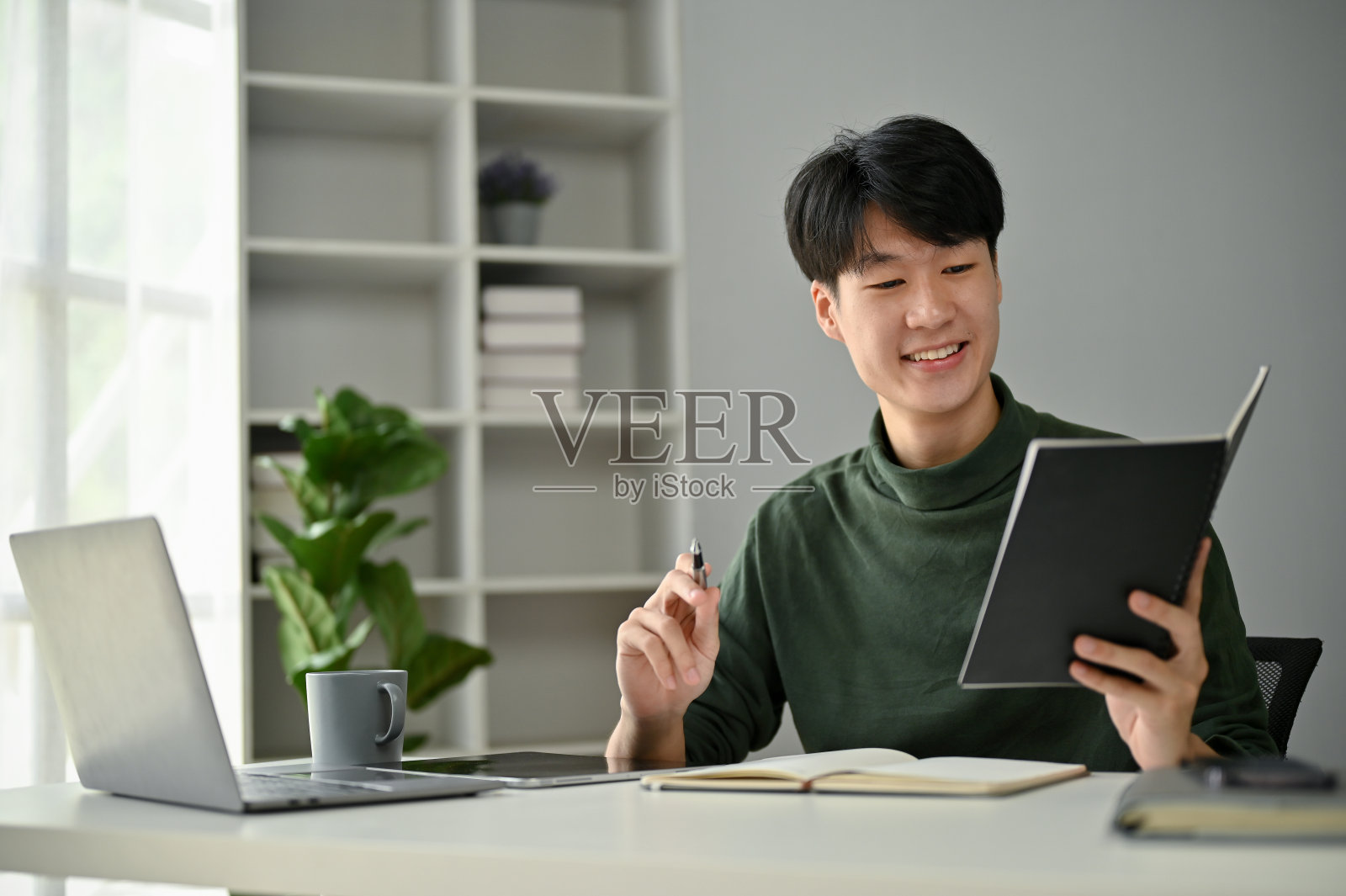 一个男人在办公桌前工作时，在他的个人计划簿上查看他的会议安排。照片摄影图片