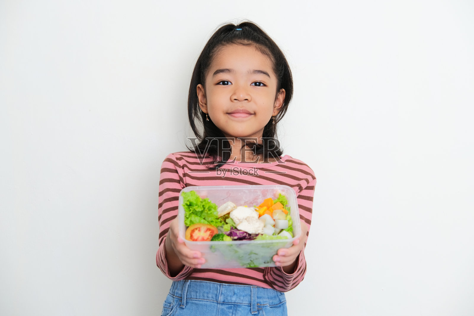 一个亚洲小孩对着镜头微笑，展示了一个装满蔬菜的盒子照片摄影图片