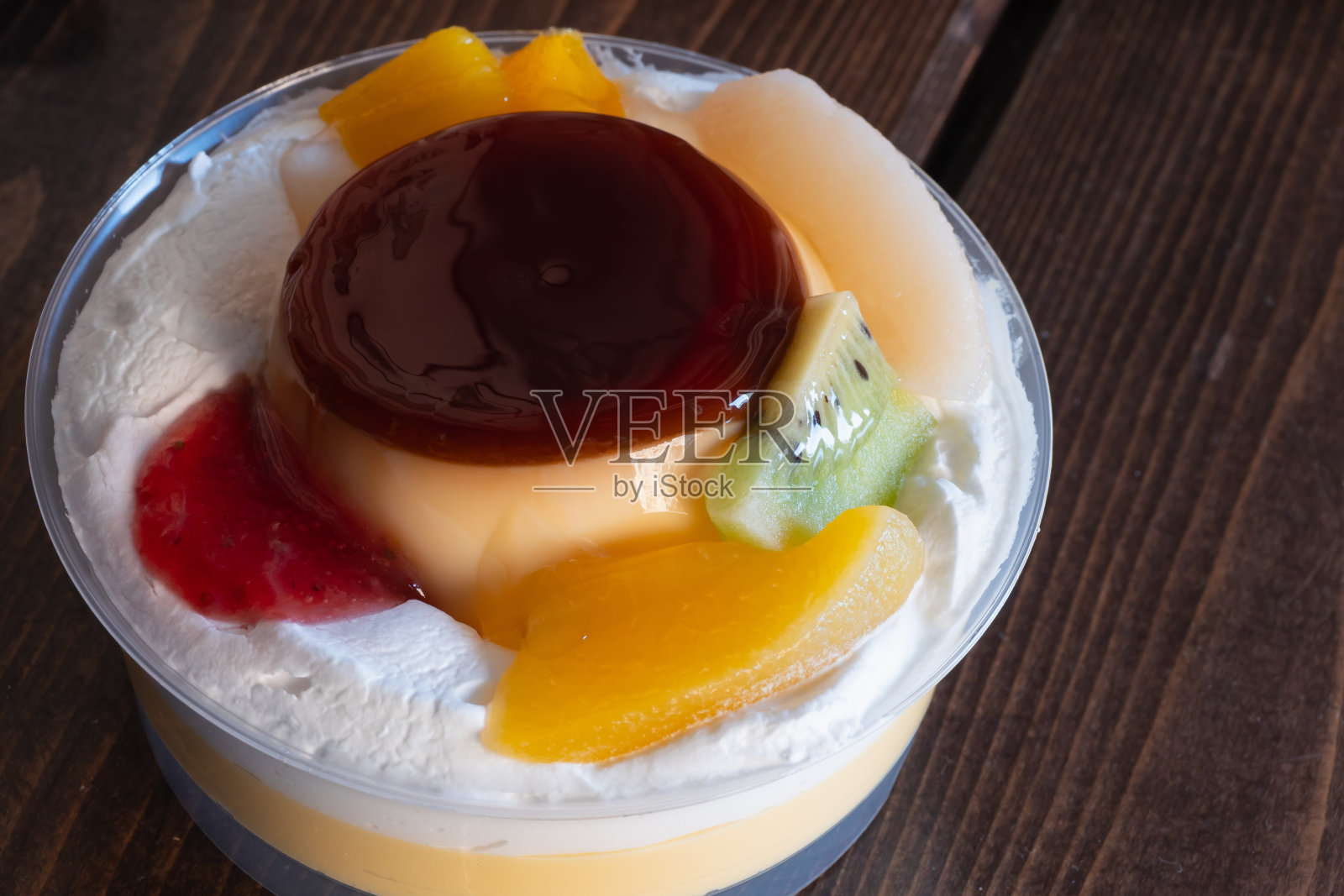 布丁放在塑料容器里。糖果上面撒上鲜奶油和水果。照片摄影图片