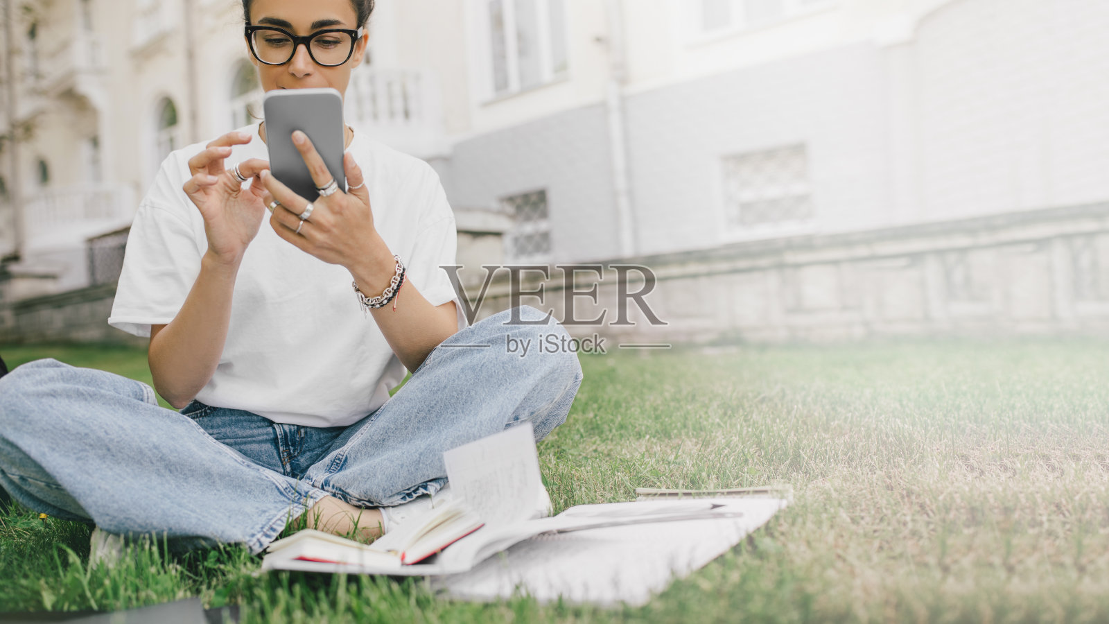年轻的女学生坐在草地上，用她的书、笔记本电脑和笔记本学习。照片摄影图片