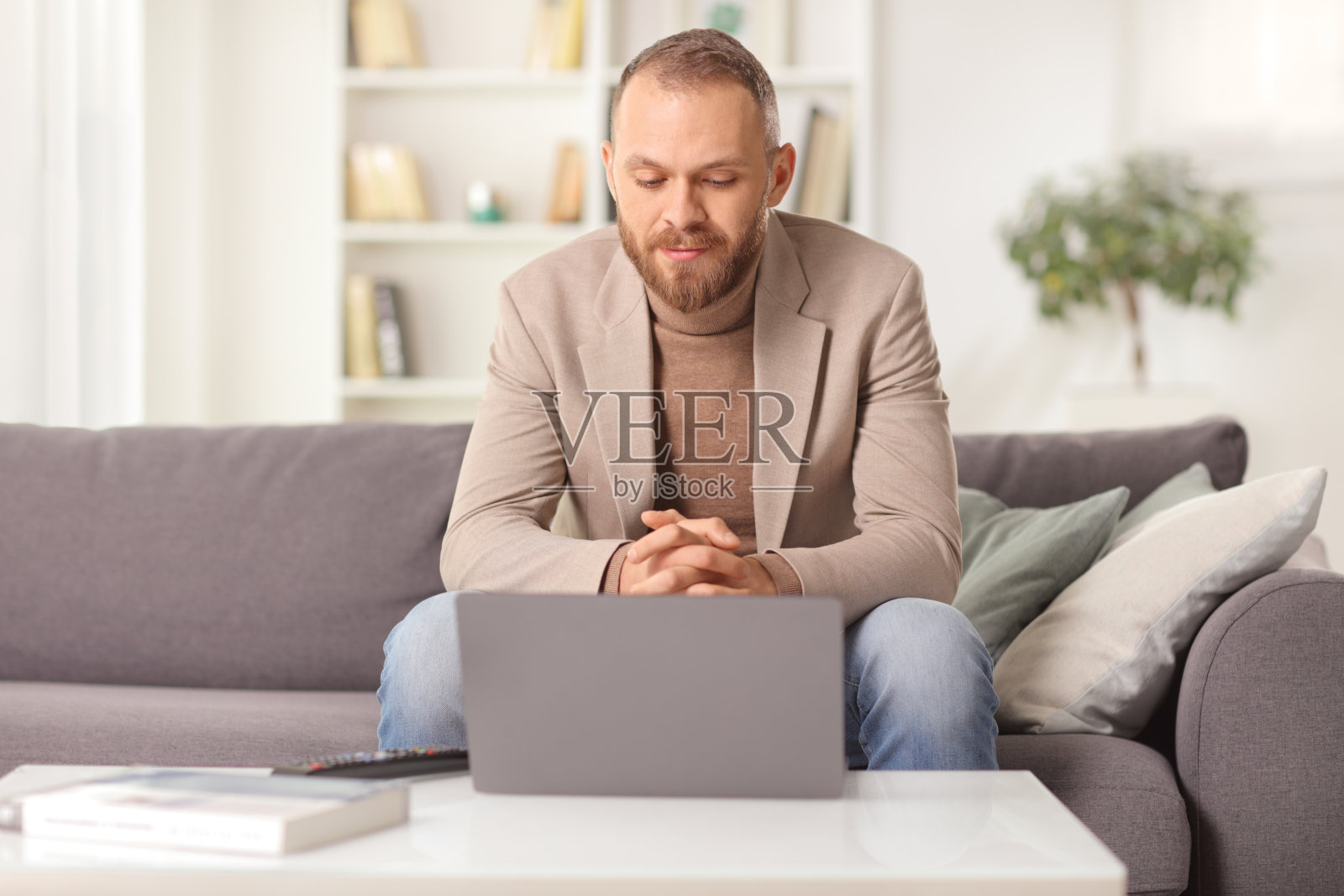 年轻人坐在家里的沙发上，看着笔记本电脑照片摄影图片