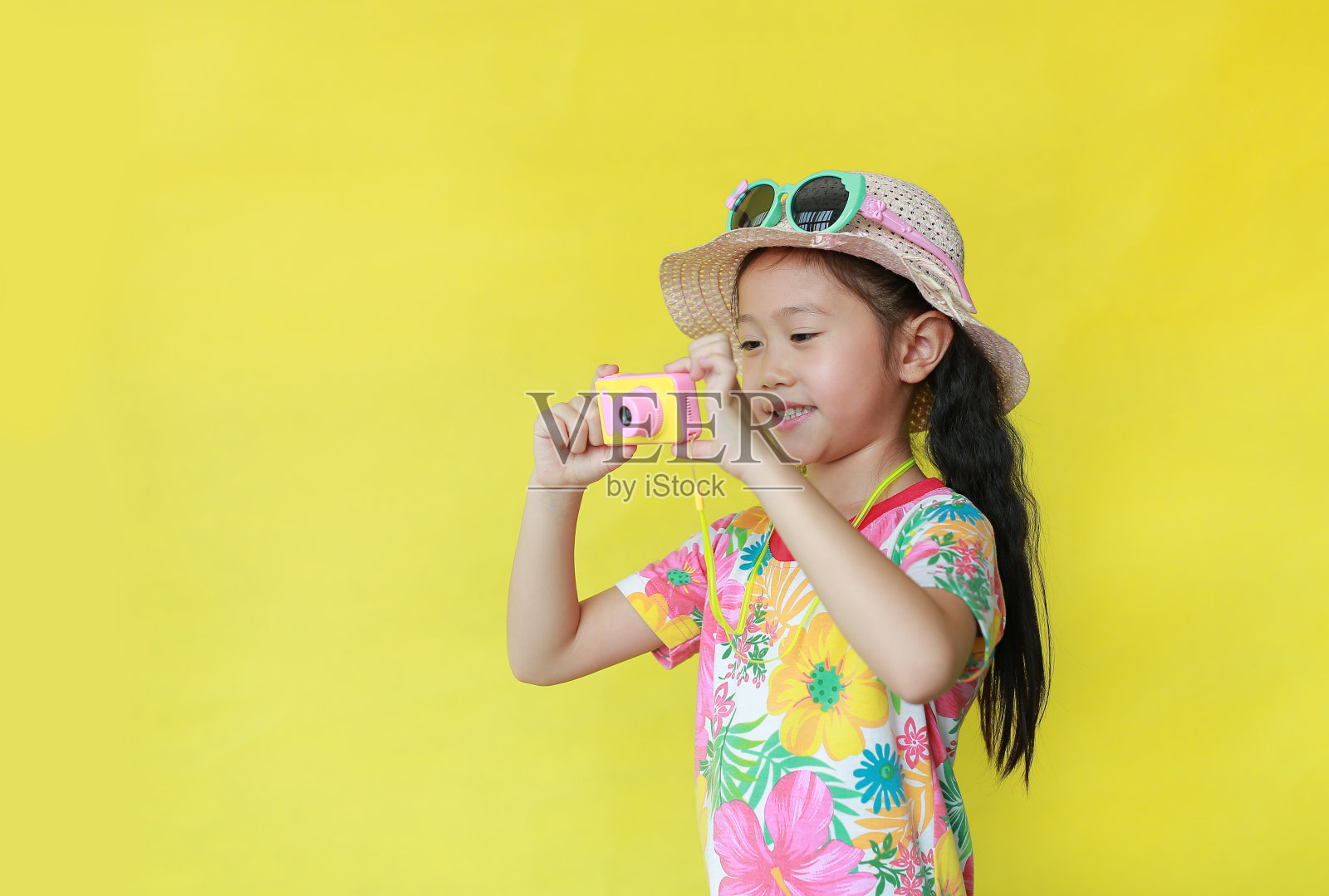 小女孩用玩具相机拍照。儿童游客穿着花图案的夏装，戴着黄色背景的帽子和太阳镜。照片摄影图片