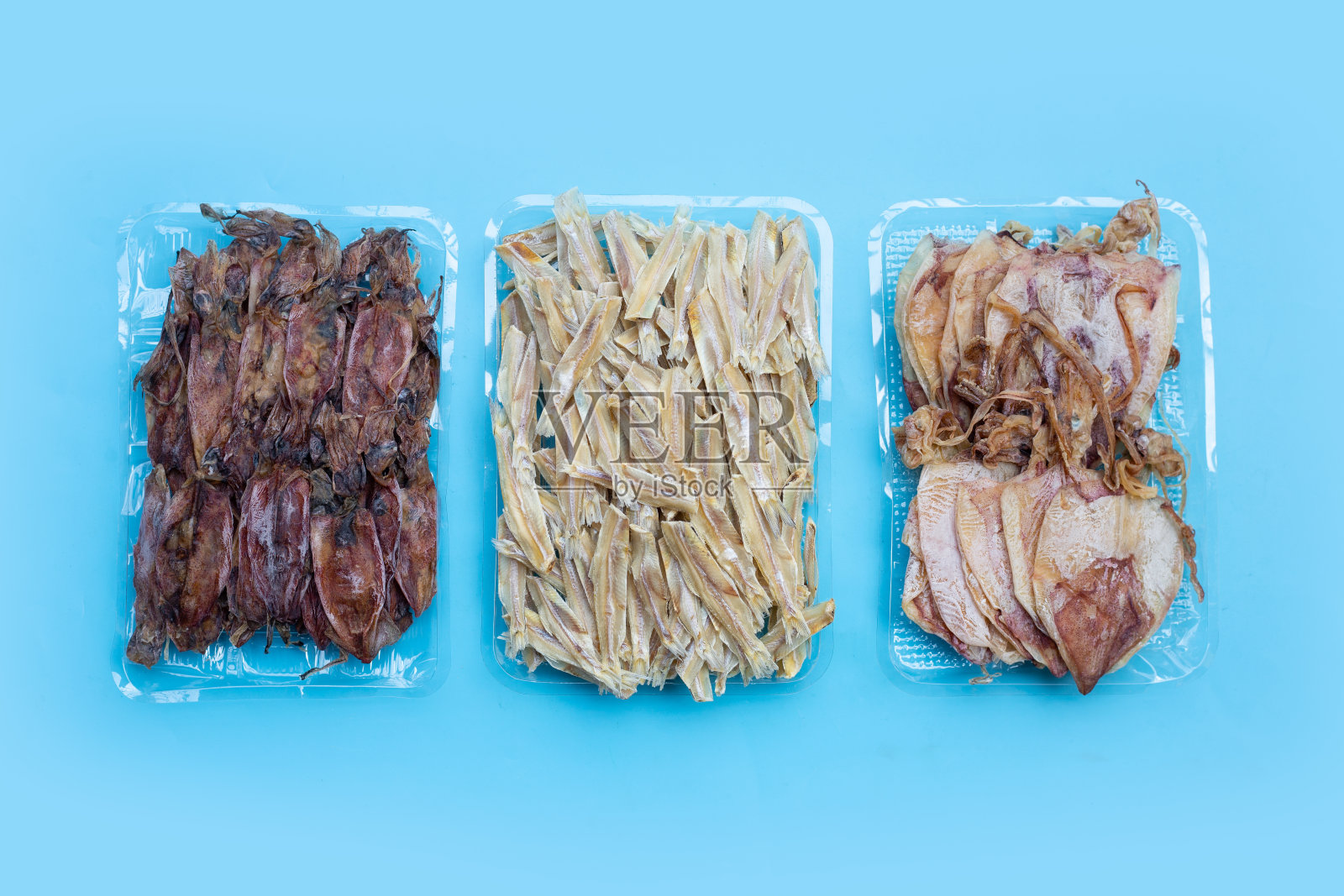 蓝色背景的干凤尾鱼和干鱿鱼。照片摄影图片