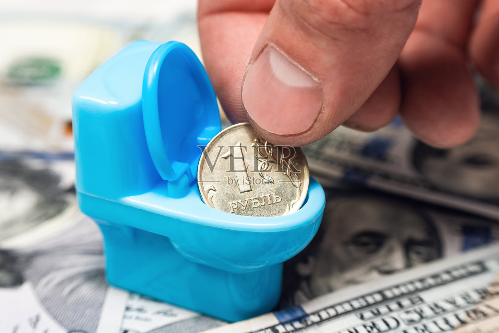 这只手把俄罗斯卢布放进一个玩具马桶里，背景是美元。贬值，卢布对美元的贬值照片摄影图片