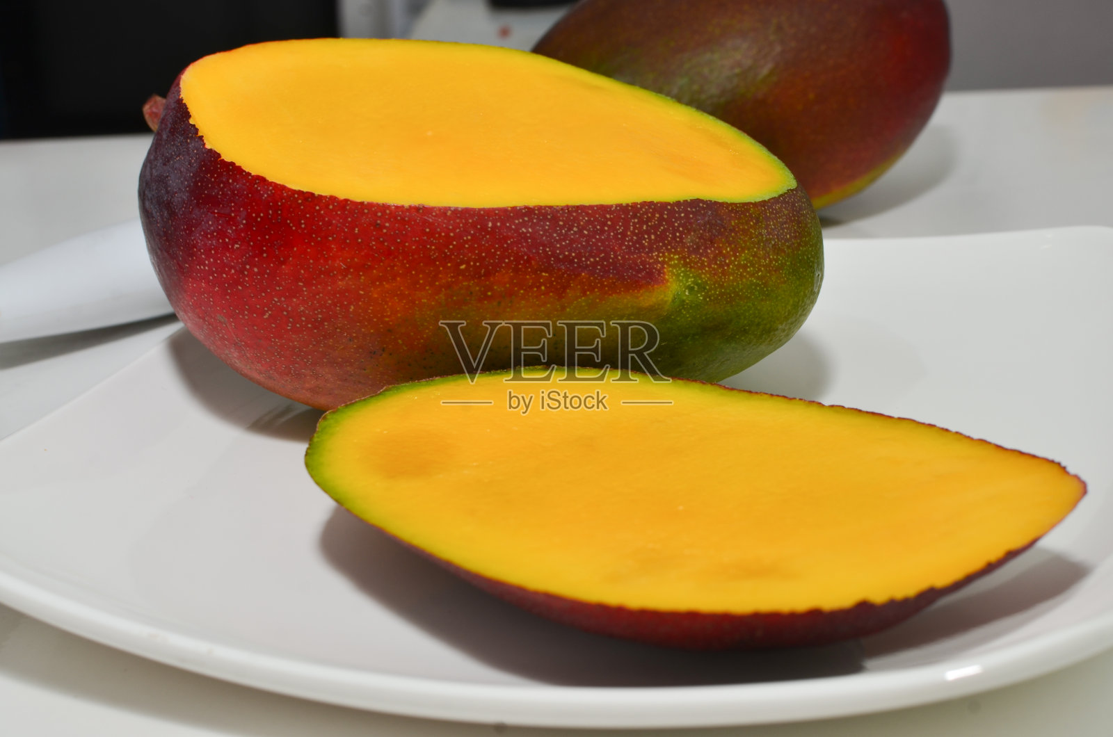 把成熟的黄色芒果切片放在白色的盘子里，就可以享用健康清爽的一餐了。照片摄影图片