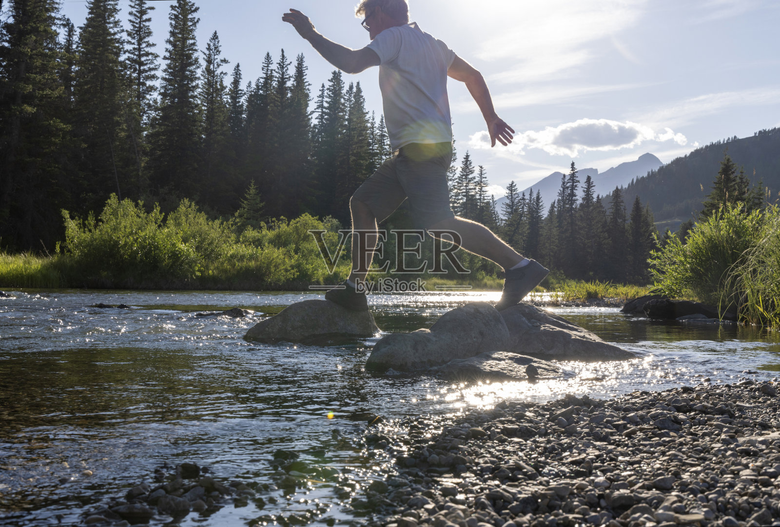 徒步旅行者在溪流中的巨石之间跳跃照片摄影图片