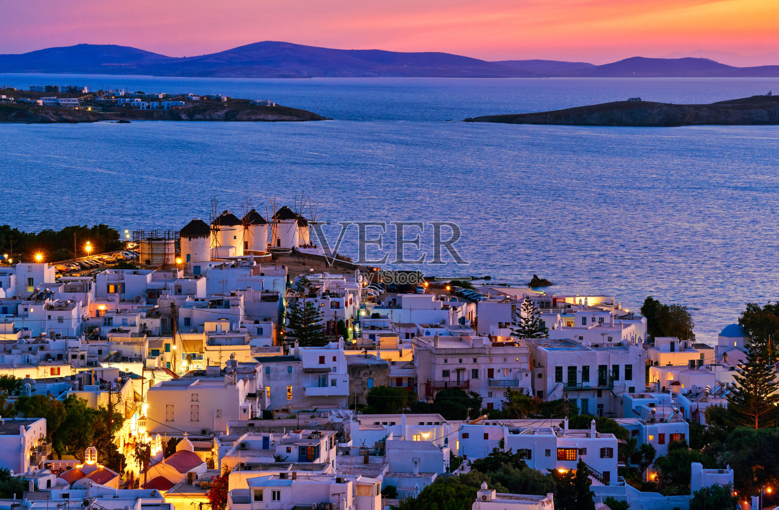 希腊基克拉迪群岛米科诺斯岛著名传统白色风车的美丽日落。粉刷过的房子，五颜六色的天空，夏日的黄昏，镇上的灯火照片摄影图片