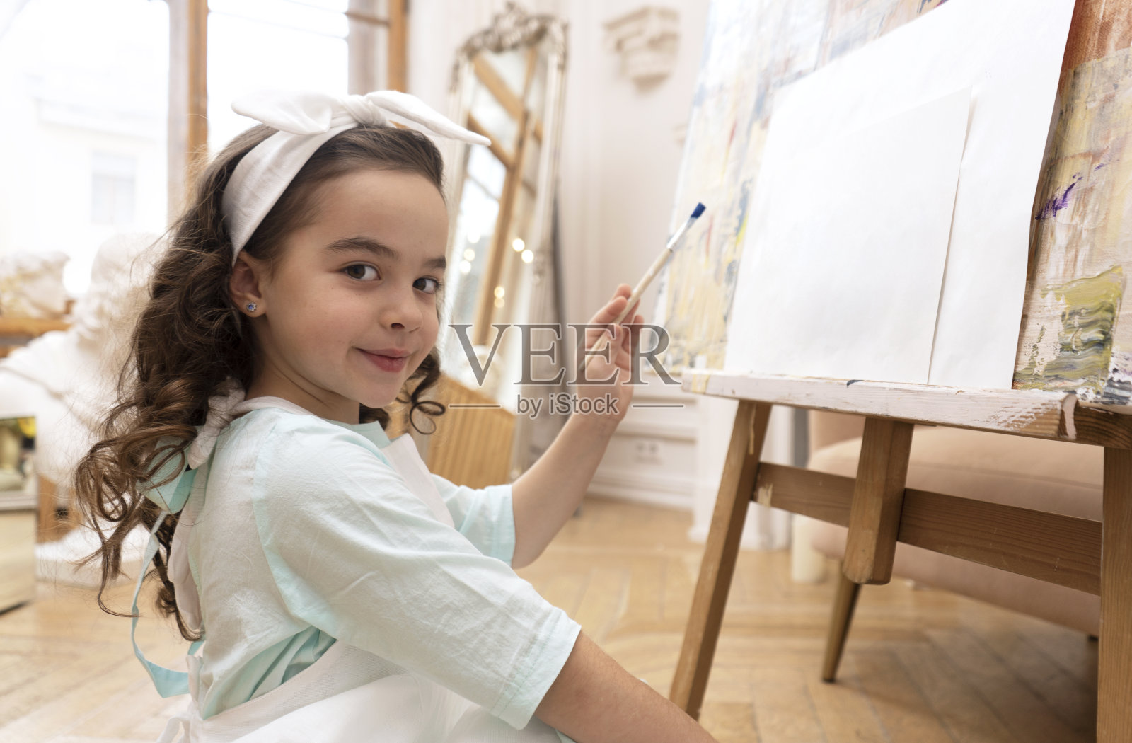 才华横溢的小艺术家看着镜头微笑，准备用画笔在画布上画画。艺术幼儿园。照片摄影图片