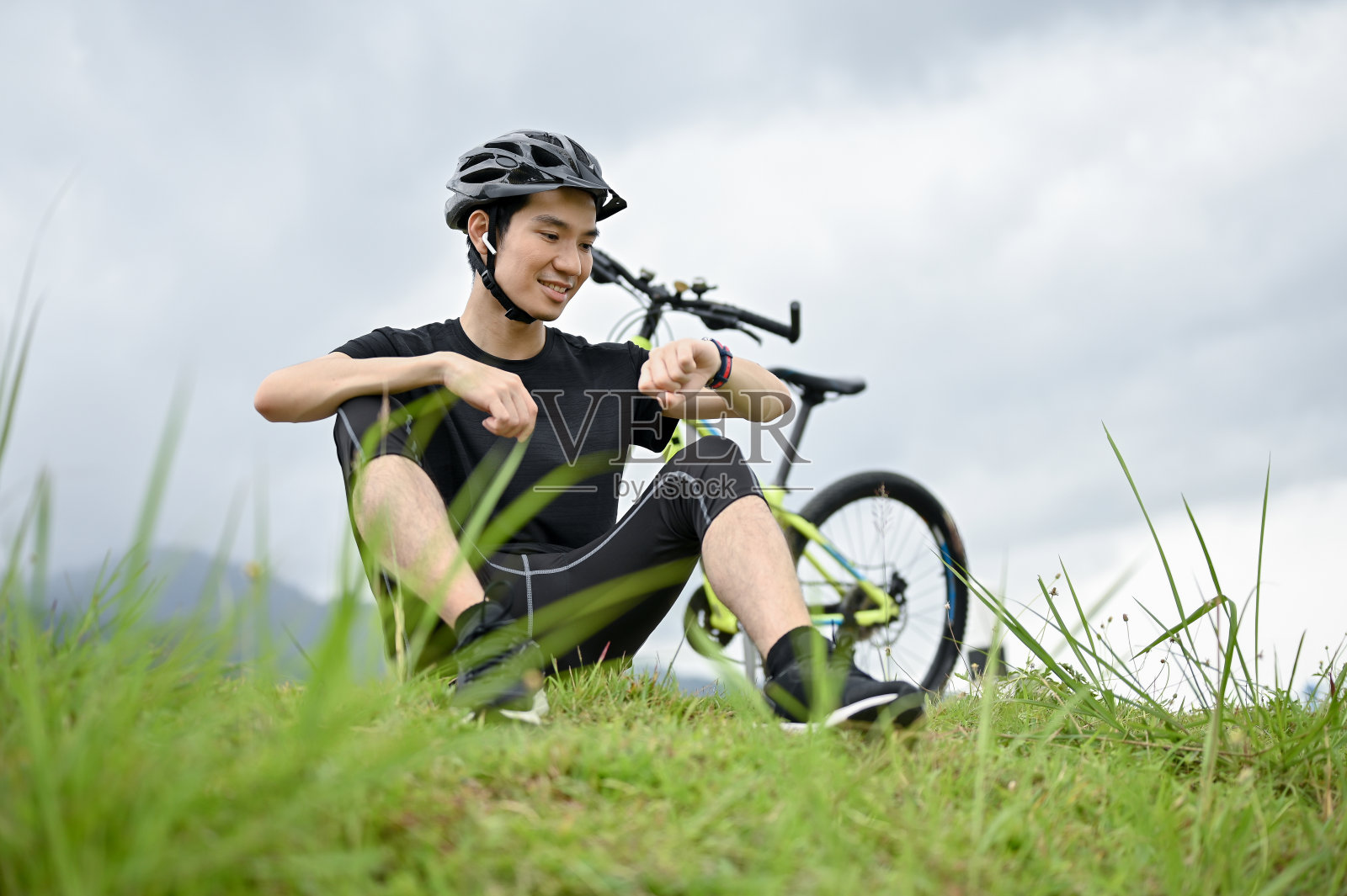一位快乐的亚洲男子躺在草地上休息时，用智能手表查看自己消耗的卡路里照片摄影图片