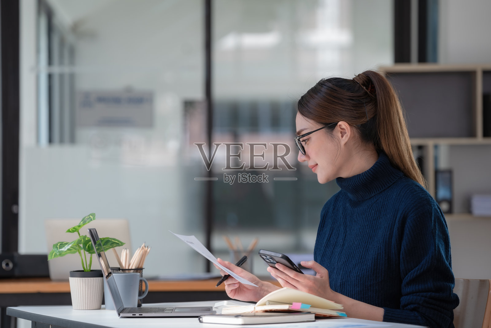 美丽的亚洲女性坐在办公桌前使用智能手机和笔记本电脑，在家工作的概念。照片摄影图片