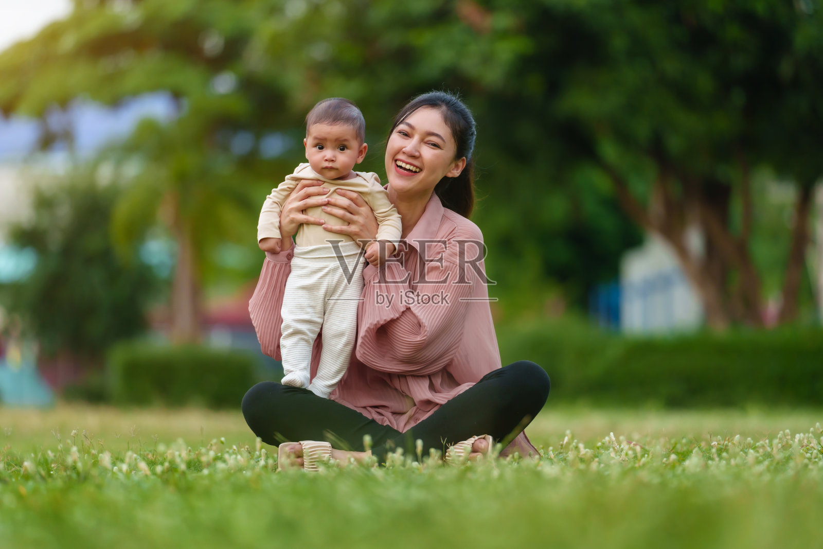 母亲抱着婴儿坐在草地上照片摄影图片
