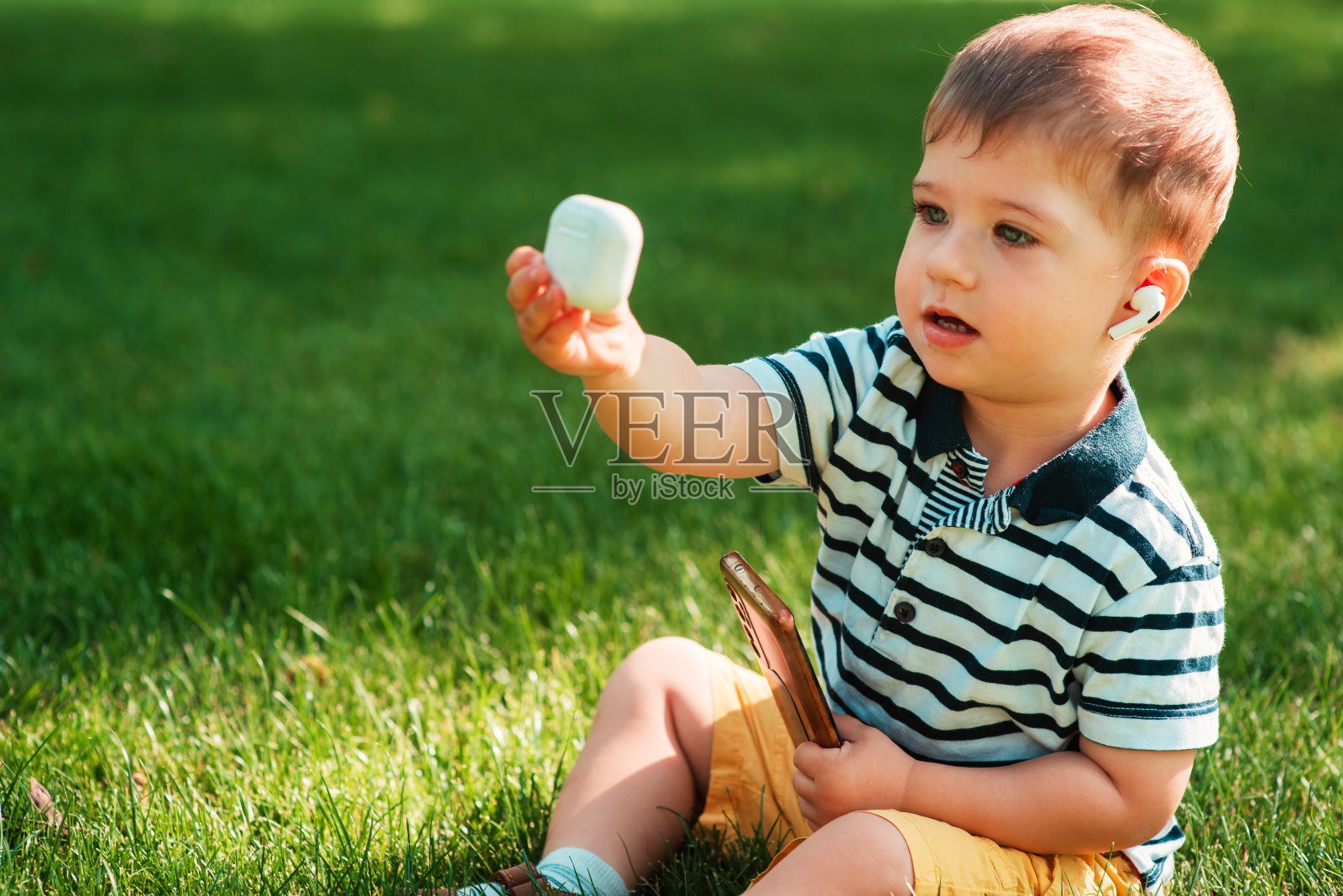 前景中，一个可爱的欧洲男孩拿着一盒无线耳机。戴无线耳机照片摄影图片