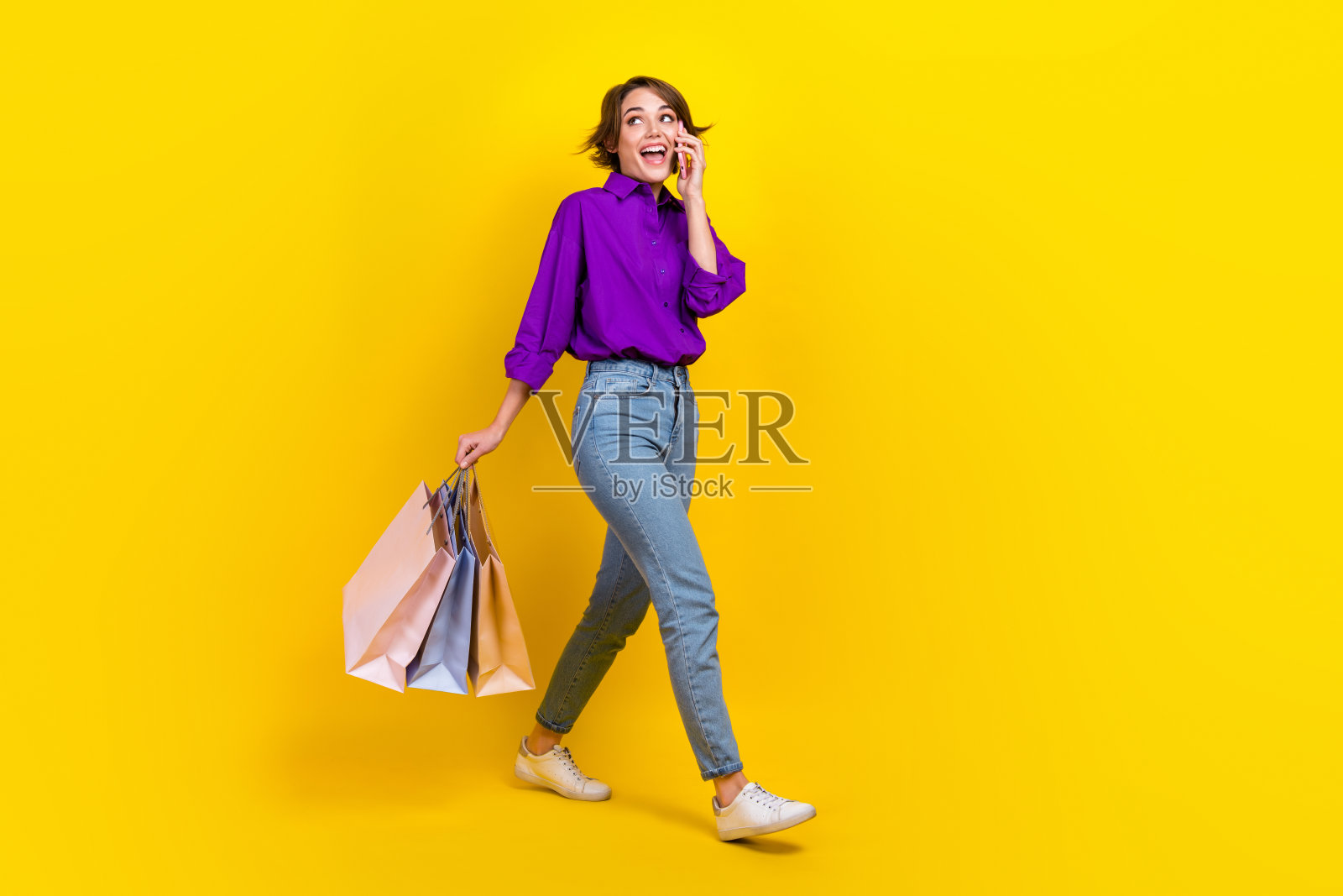 年轻女子的全身照片，穿着时尚的正式制服，拿着精品包，电话称赞孤立在黄色背景照片摄影图片