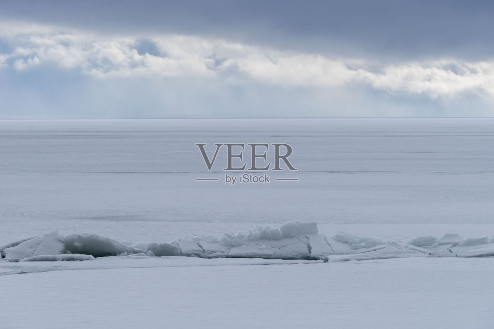 在一小块结冰的水面上，有几处雪堆，积雪正在融化照片摄影图片