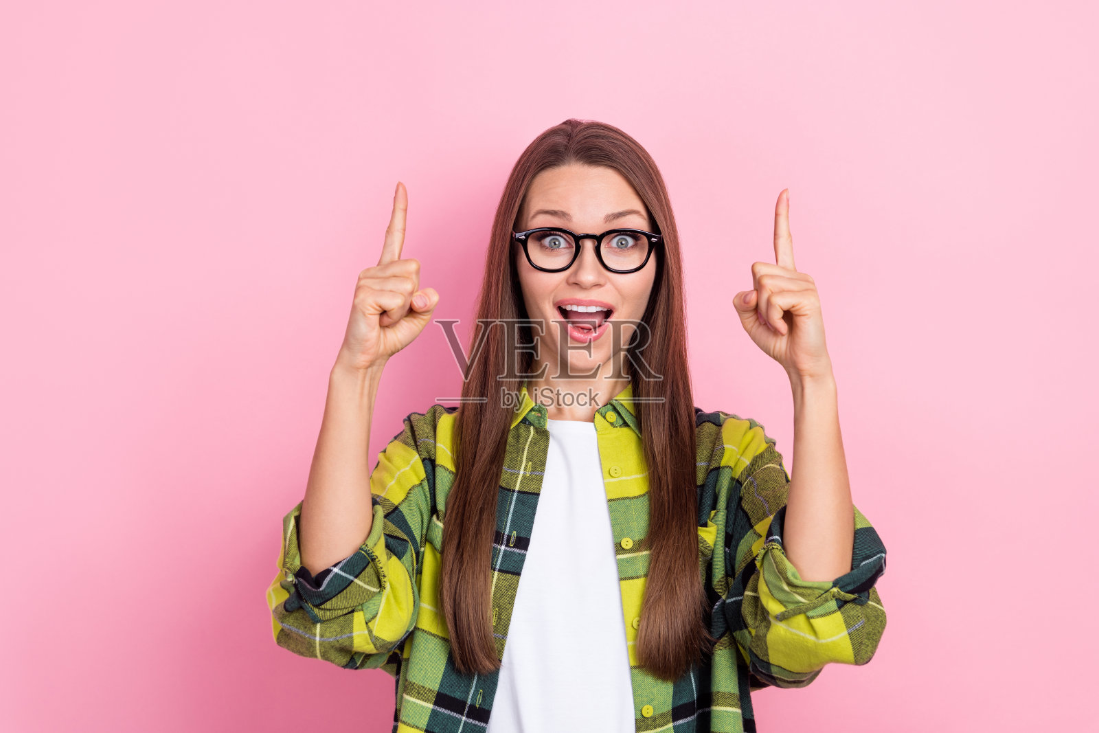 照片中，惊讶而欢快的女士张开嘴，手指直接指向粉红色背景上的空白空间照片摄影图片