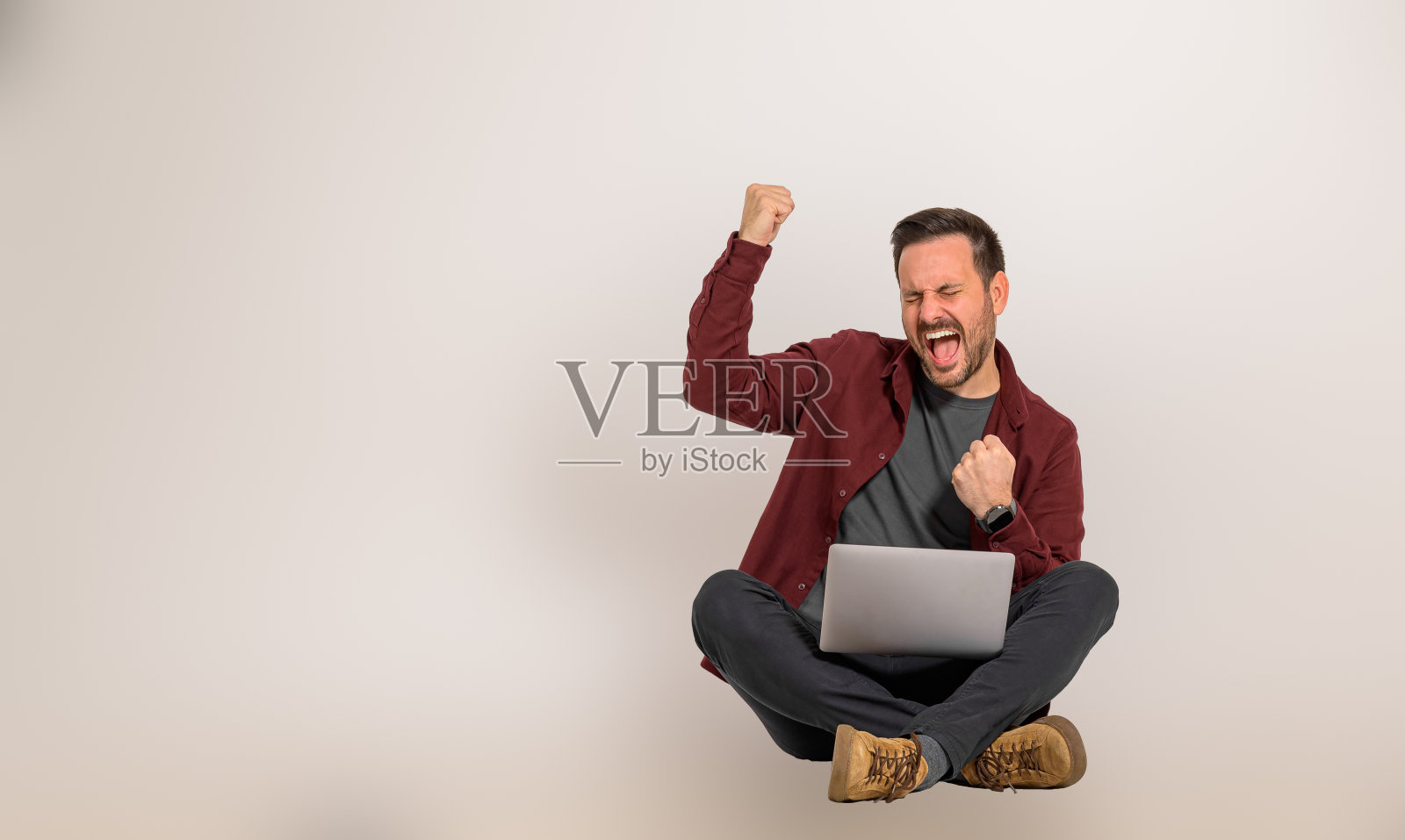 成功的商人闭着眼睛狂喜地尖叫，挥舞着拳头。欢快的销售经理坐在笔记本电脑前庆祝胜利照片摄影图片