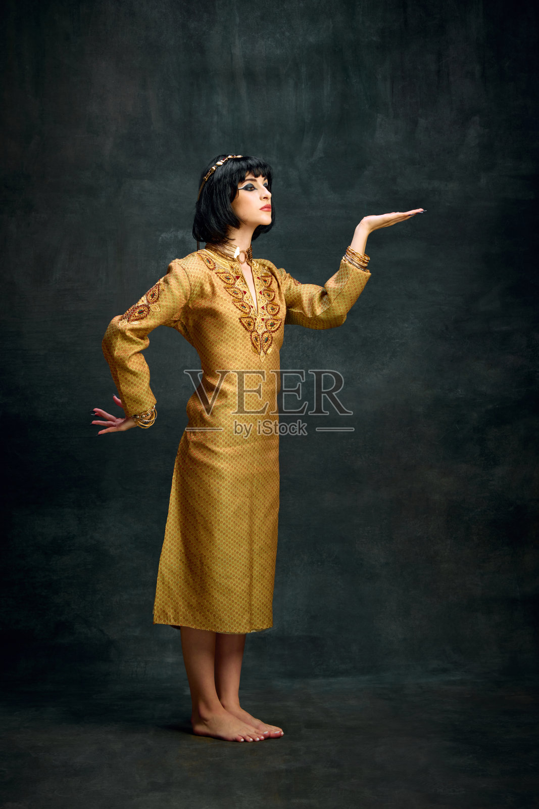 身穿金色长裙的年轻女子的肖像，埃及女王克利奥帕特拉在黑暗的复古背景下摆姿势。皇家的人照片摄影图片