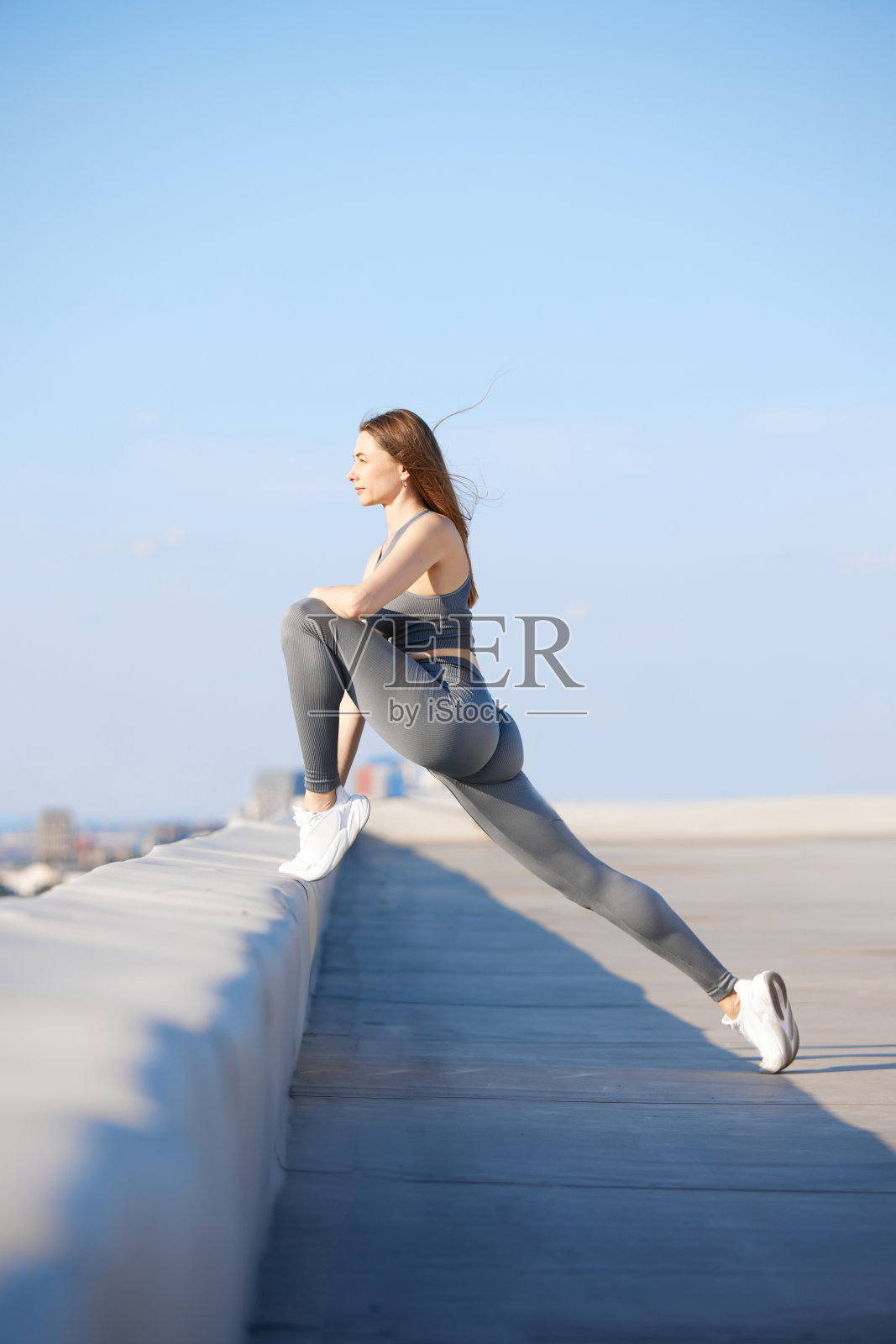 柔韧性和力量。年轻的运动女性穿着时尚的运动服训练，在阳光明媚的日子里在户外做伸展运动照片摄影图片