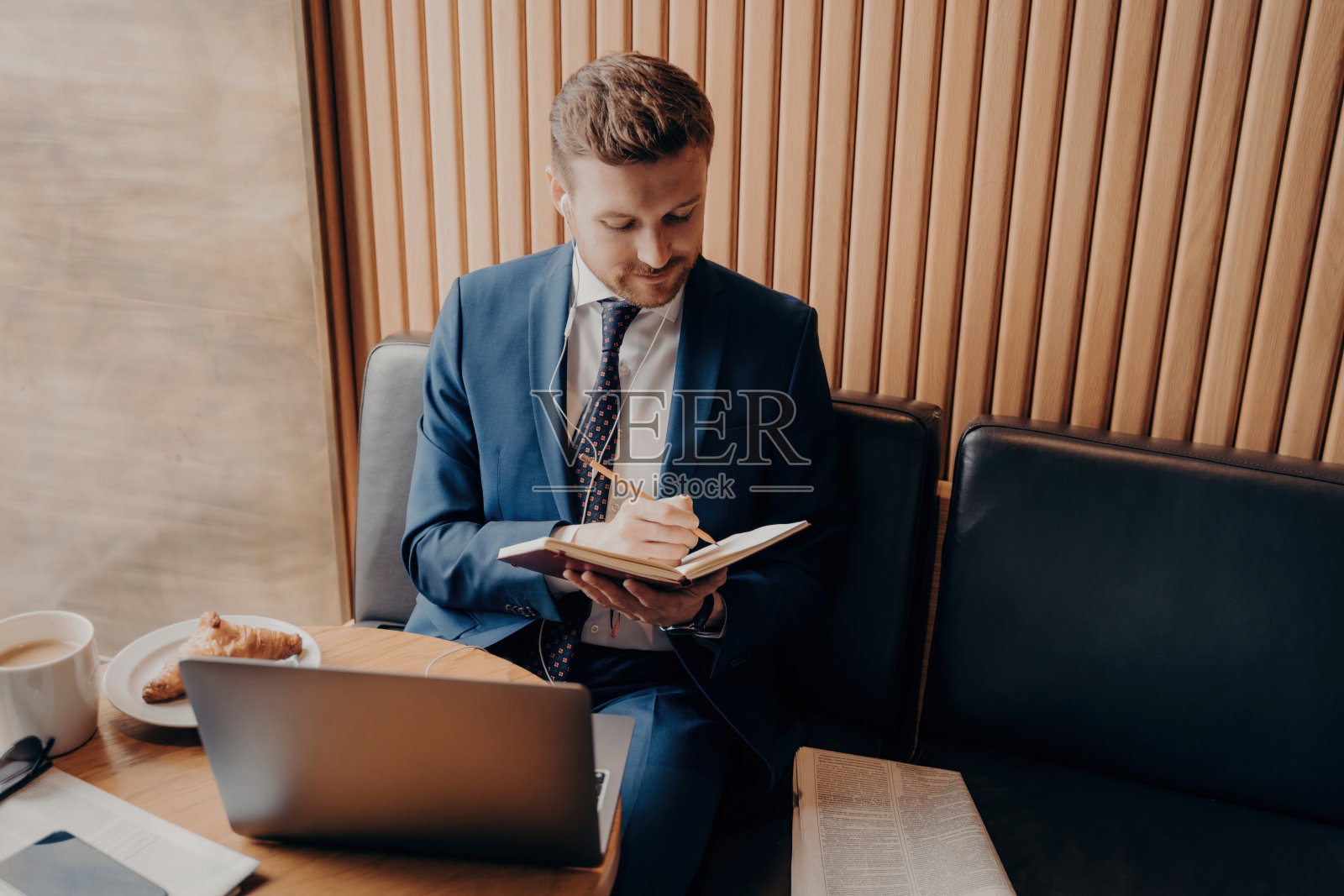 穿着正装的大胡子商人记笔记，在咖啡馆用笔记本电脑听在线讲座，在早餐时远程工作。照片摄影图片