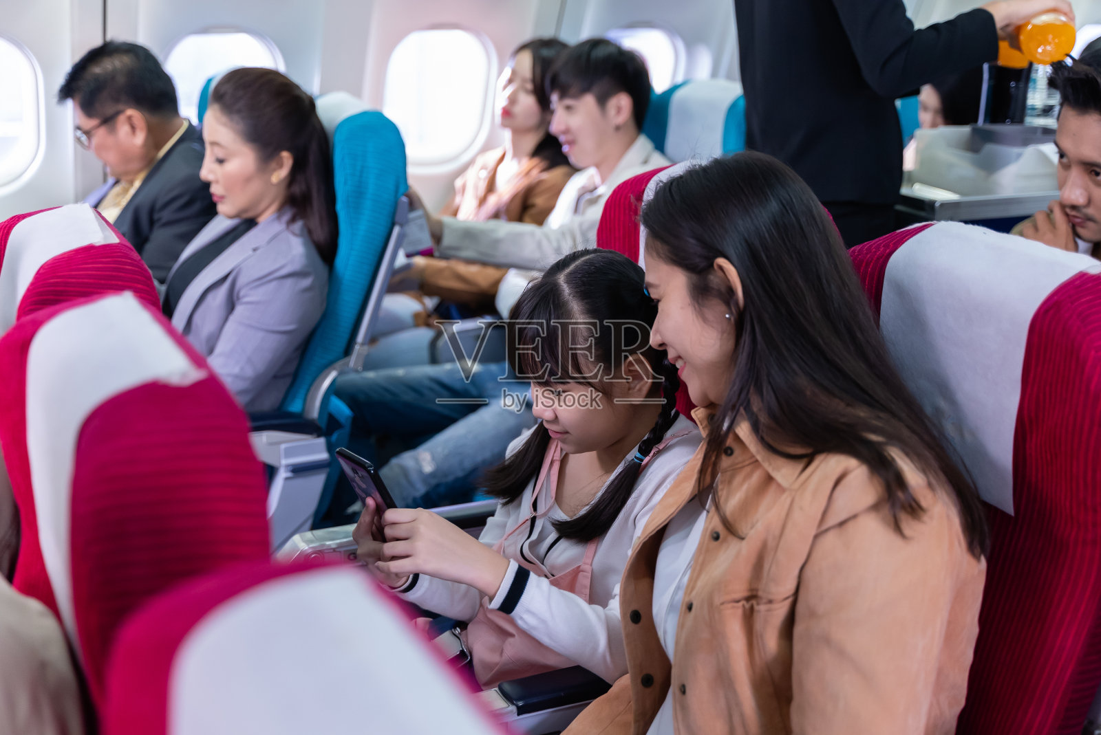 亚洲旅客旅行团乘飞机出国旅游。年轻的亚洲女孩坐在飞机座位上用智能手机和妈妈自拍。家庭旅游旅游度假概念。照片摄影图片
