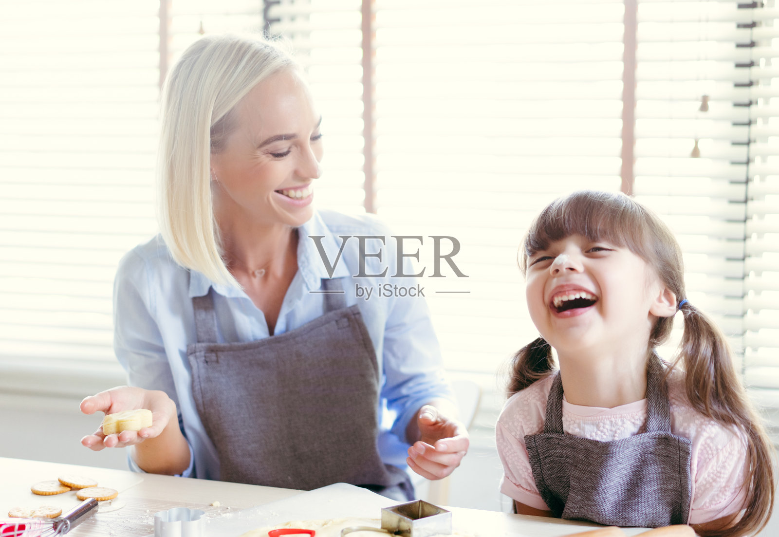 快乐的母女俩在家里的餐桌上一边揉面一边嬉笑，一边做星形饼干。微笑的家庭烹饪美味的饼干。照片摄影图片