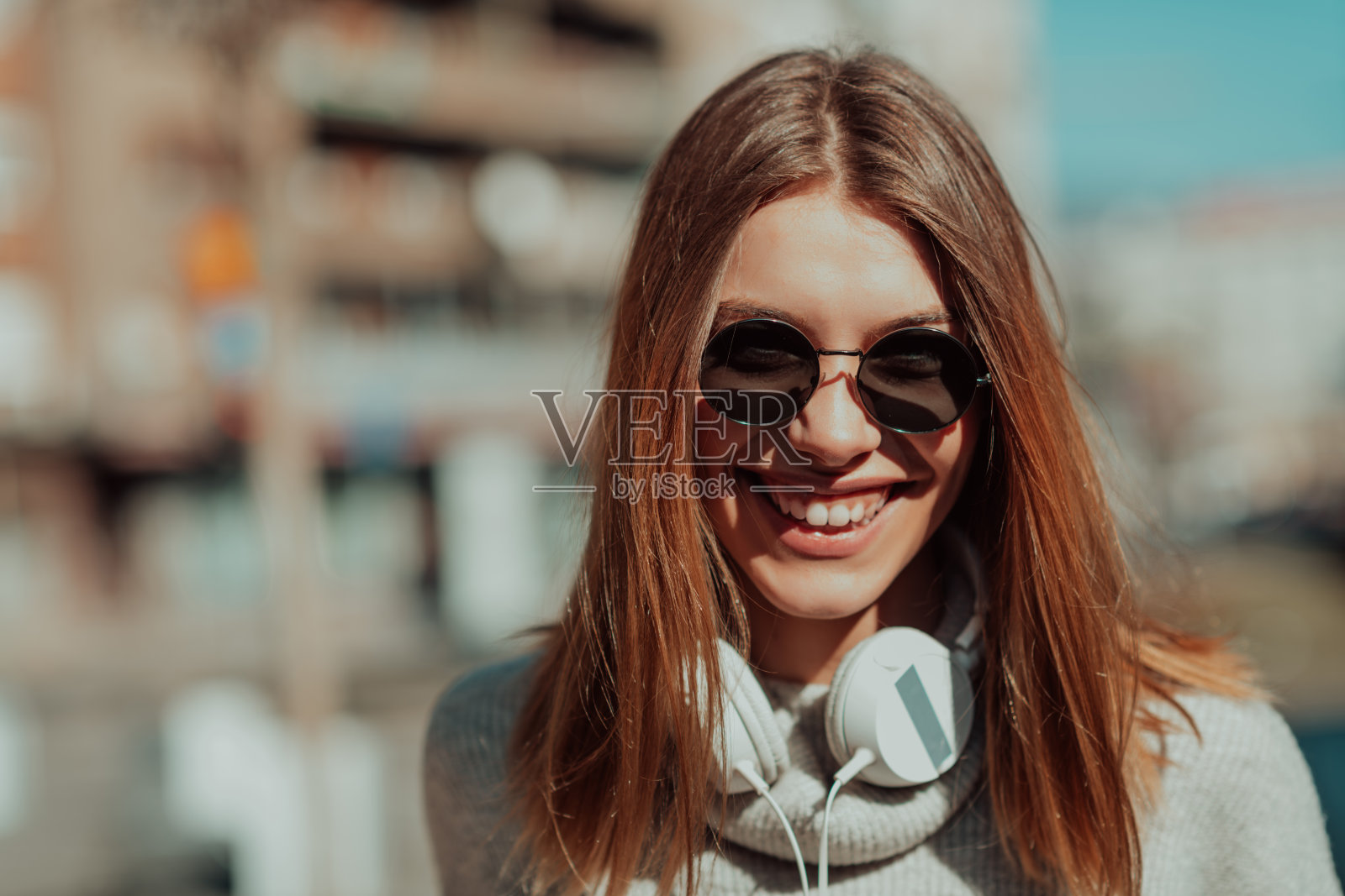 一个戴着墨镜的现代女孩走在街上，戴着耳机听音乐。照片摄影图片