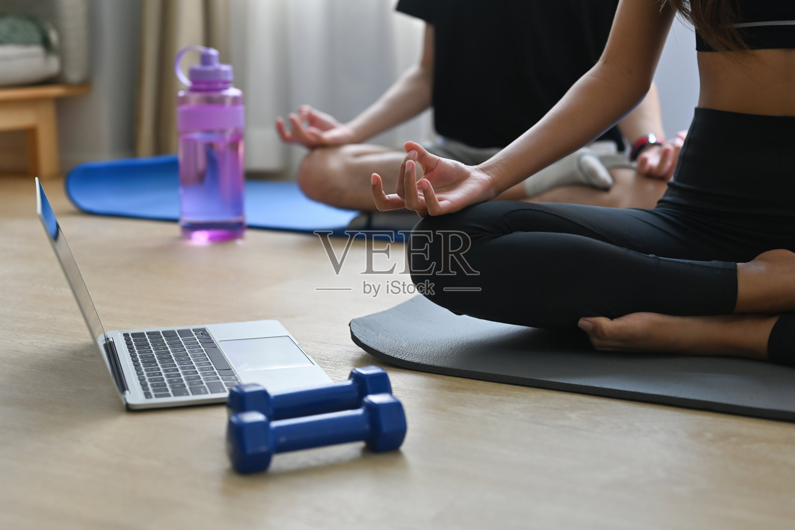 一个健康的男人和一个女人盘腿坐在瑜伽工作室的垫子上冥想，旁边有哑铃和笔记本电脑，用于家庭锻炼，冥想和在线瑜伽概念。照片摄影图片