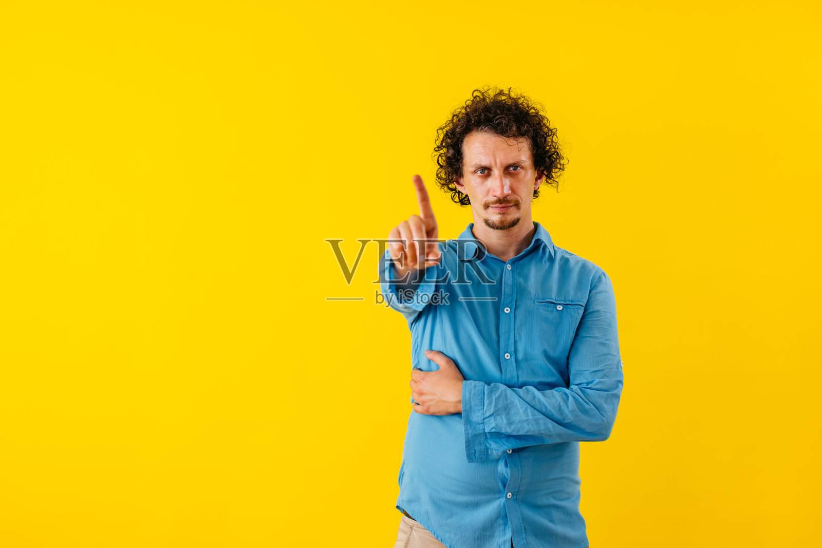 不满的年轻人在黄墙前挥动手指照片摄影图片