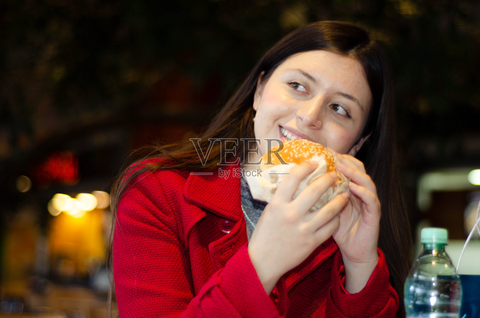 美丽快乐开朗的女孩，年轻积极的女人坐在购物中心的美食广场上，手里拿着多汁的大汉堡，汉堡包，薯条，微笑着。快餐、垃圾、不健康的快餐。照片摄影图片