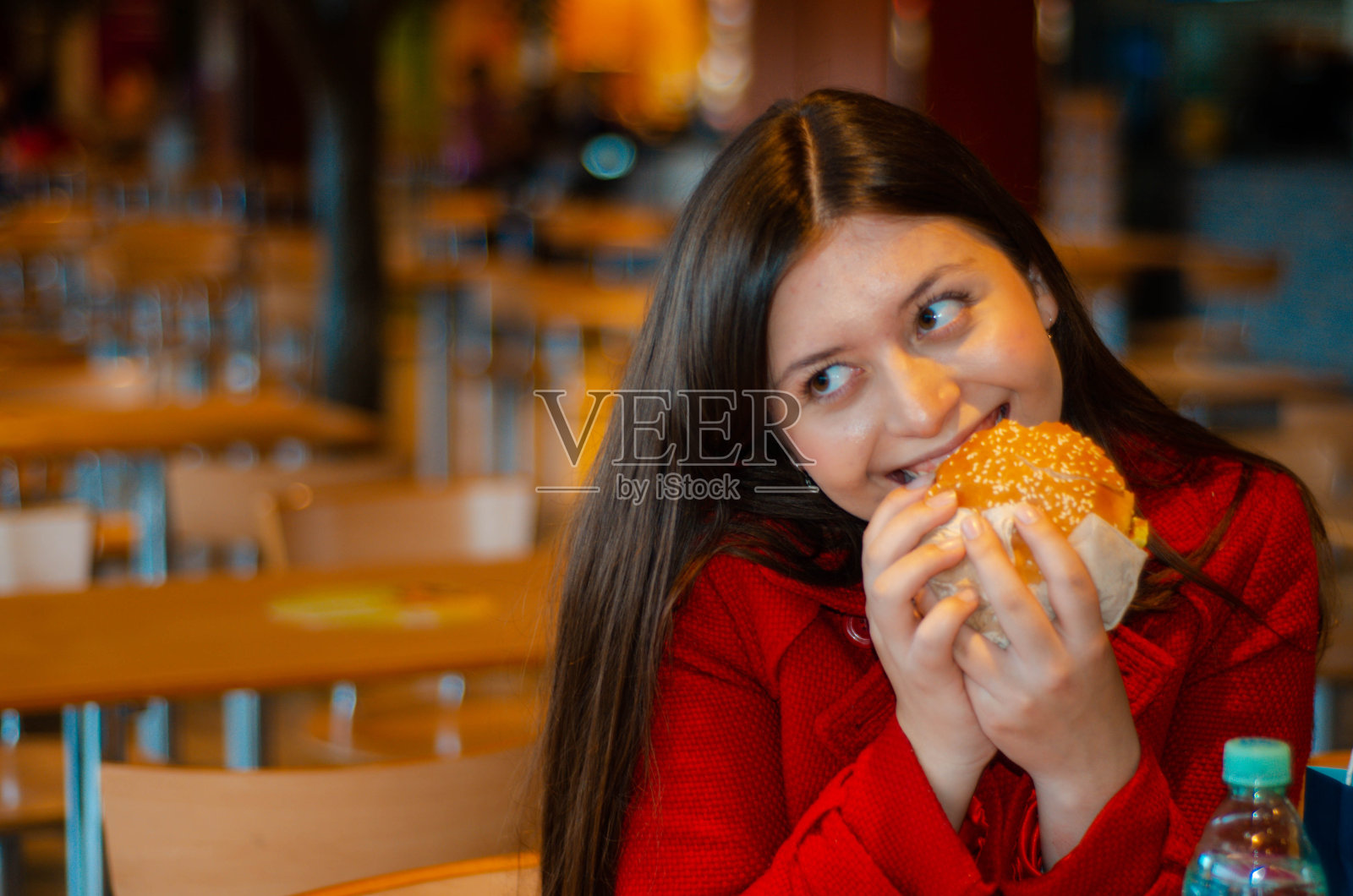 美丽快乐开朗的女孩，年轻积极的女人坐在购物中心的美食广场上，手里拿着多汁的大汉堡，汉堡包，薯条，微笑着。快餐、垃圾、不健康的快餐。照片摄影图片