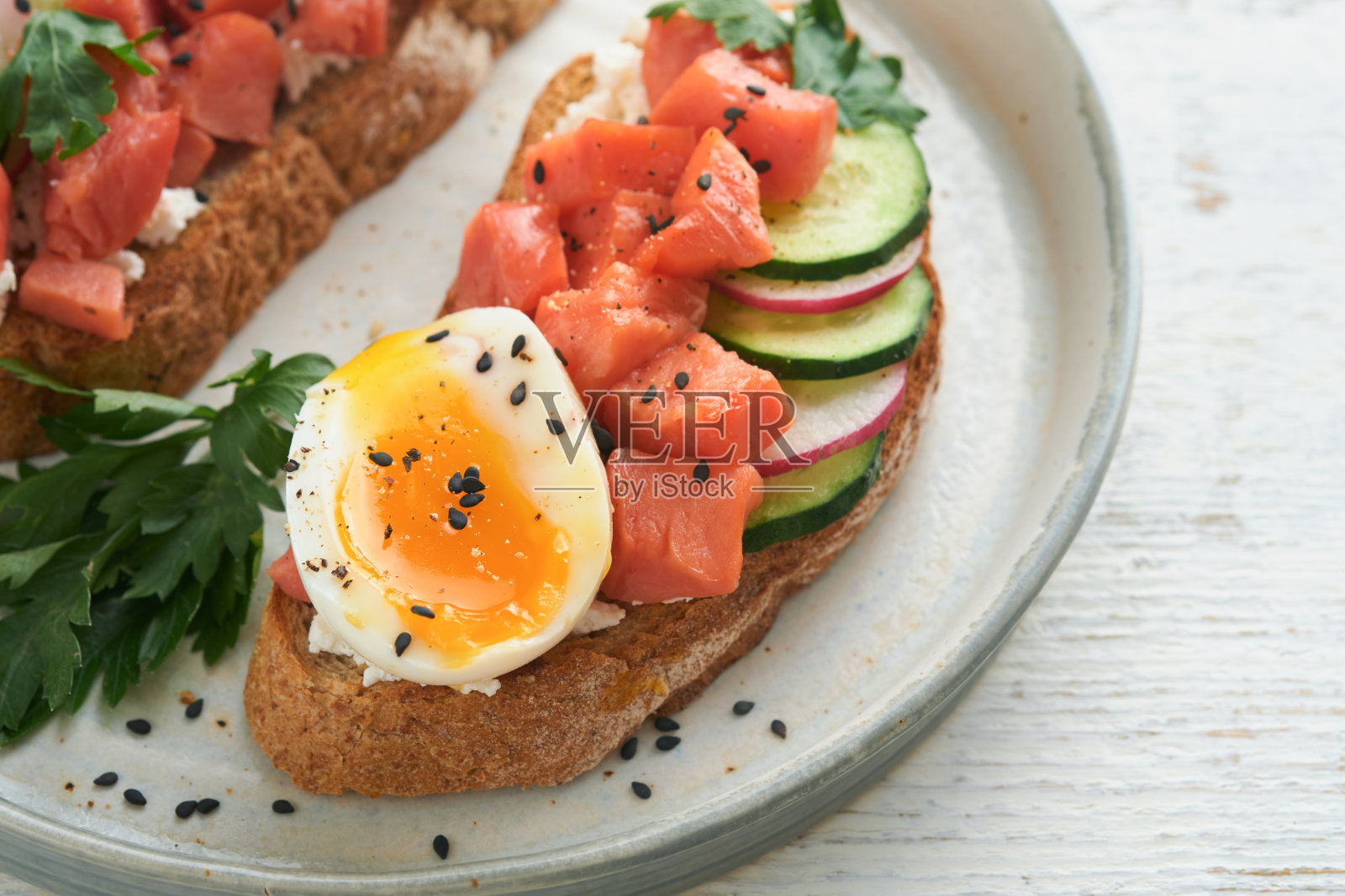 健康的三明治，面包或吐司，烟熏鲑鱼，软蛋，奶油奶酪，黄瓜，萝卜，黑芝麻和欧芹放在旧木桌上。美味的蛋白质鱼三明治早餐。Smorrebrod。照片摄影图片