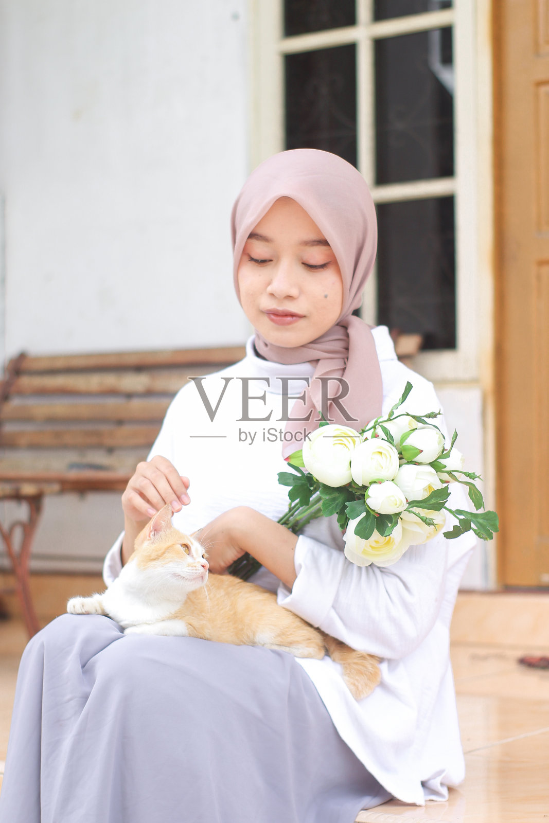 年轻的女人在房子前面和一只宠物猫玩耍照片摄影图片