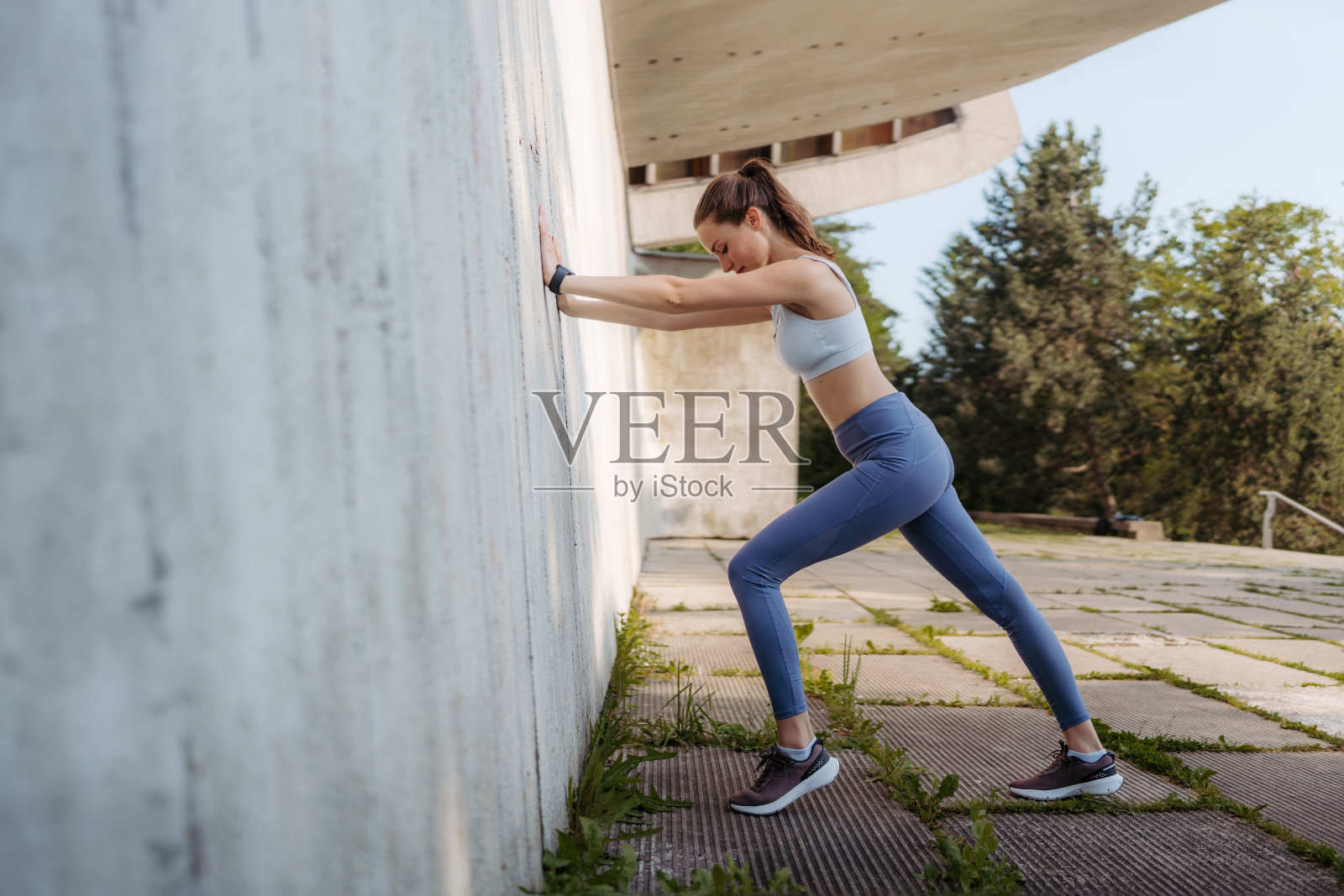 穿着运动服的年轻运动女性在城市水泥墙前锻炼的肖像。照片摄影图片