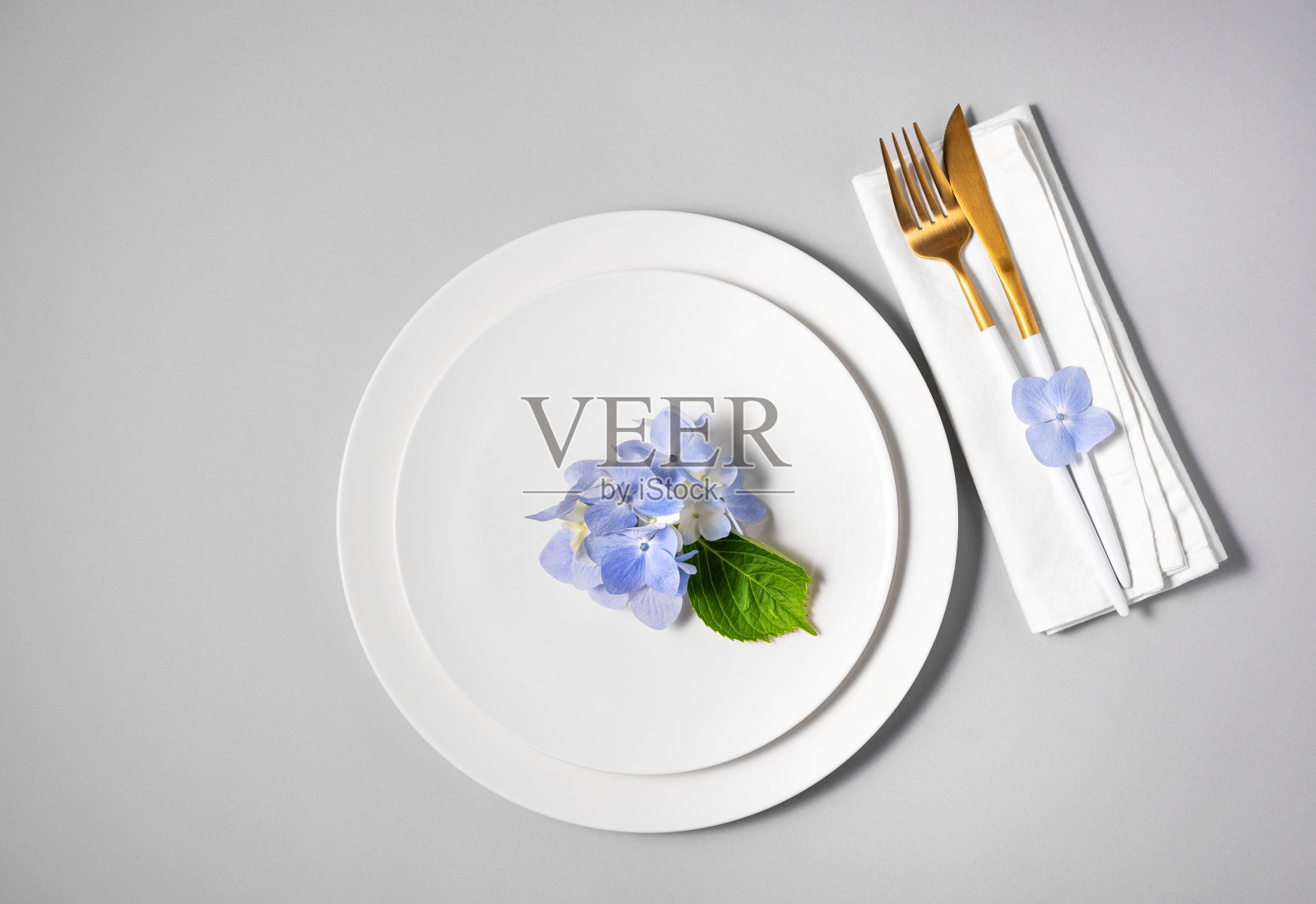 节日餐桌上的白色盘子上有蓝色绣球花，灰色背景上有餐巾和餐具。庆祝妇女节、生日或母亲节的概念。照片摄影图片