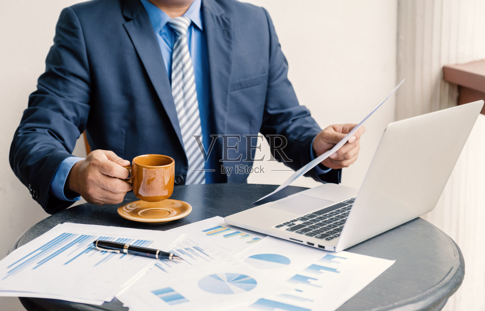 商人手持咖啡杯，在家庭办公室用笔记本电脑分析图表，设定具有挑战性的商业目标，并计划实现新的目标照片摄影图片