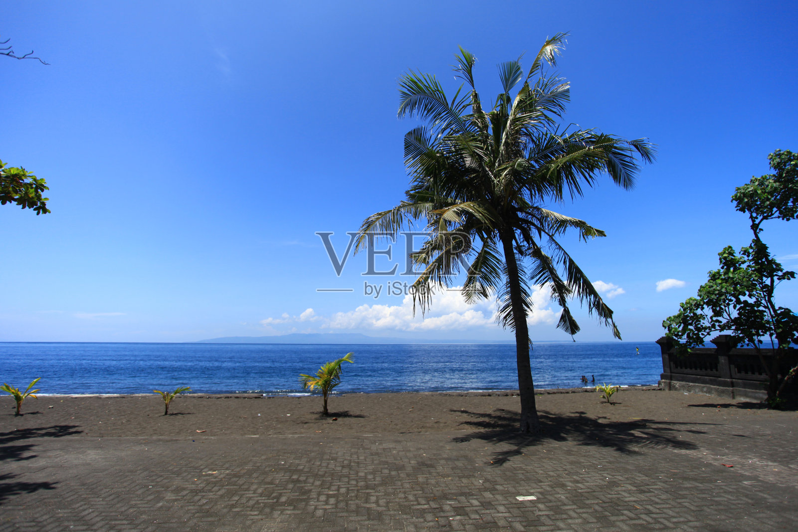 果阿拉瓦海滩在巴厘岛的一个空的黑色沙滩，椰子树，蓝天，蓝色的大海和努沙伦邦根岛在地平线上。眼前一个人也没有。照片摄影图片