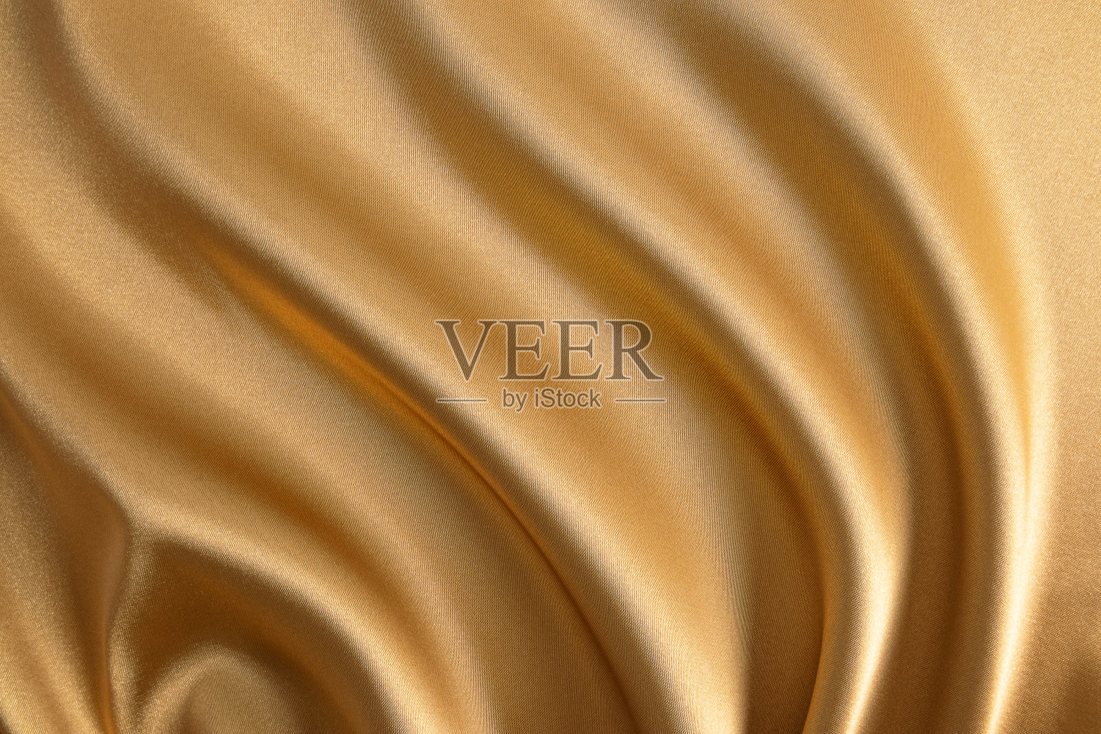 抽象的金色缎面背景豪华的织物。柔软柔软的波浪织物。织物的金色质感。喜庆，新年的背景。照片摄影图片