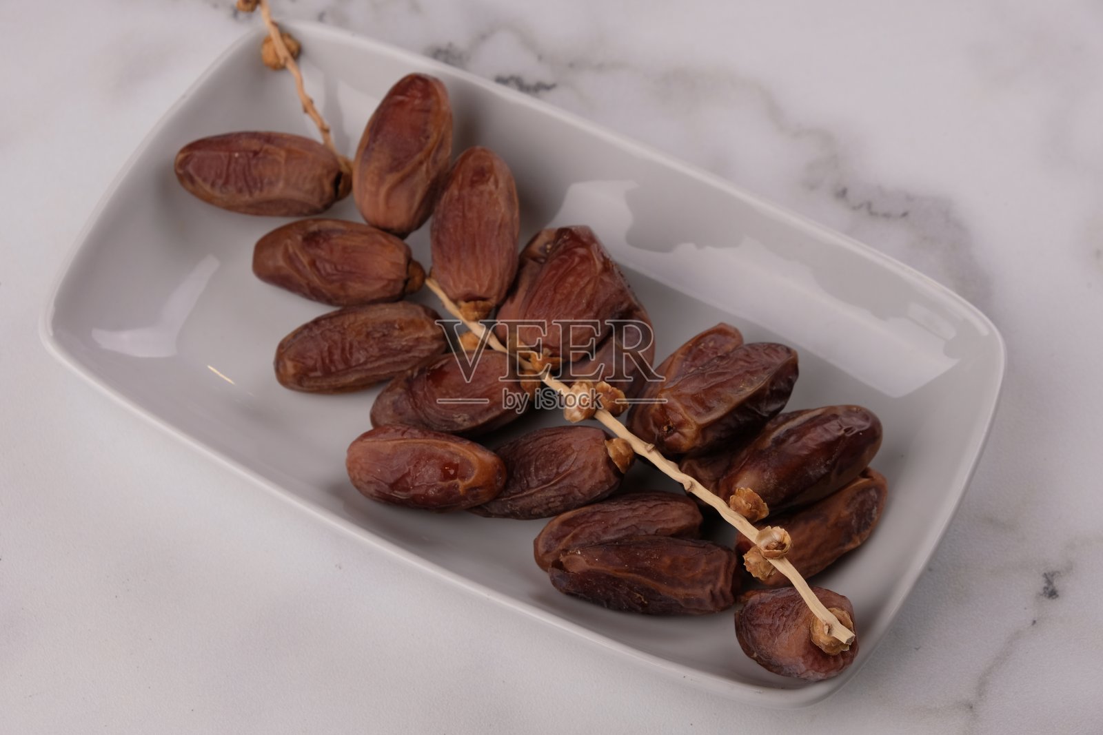 白色大理石桌子上，白色方形陶瓷盘子上的枣子。斋月开斋菜。进去tangkai。突尼斯的日期。取消约会。照片摄影图片