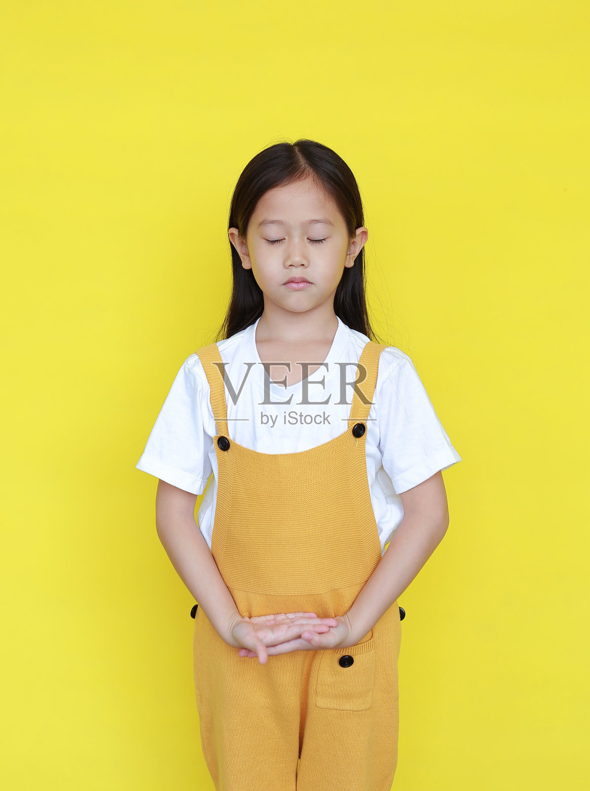 安静的亚洲小女孩闭着眼睛孤立地站在黄色背景上。冥想中的小孩表情照片摄影图片