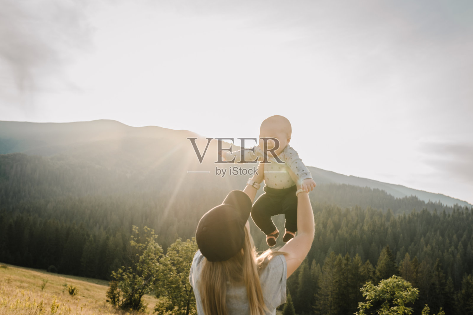 妈妈和宝宝在山上玩耍。母亲用双手把快乐的儿子抛向天空。秋日漫步大自然。一家人一起度假。世界旅游日。照片摄影图片