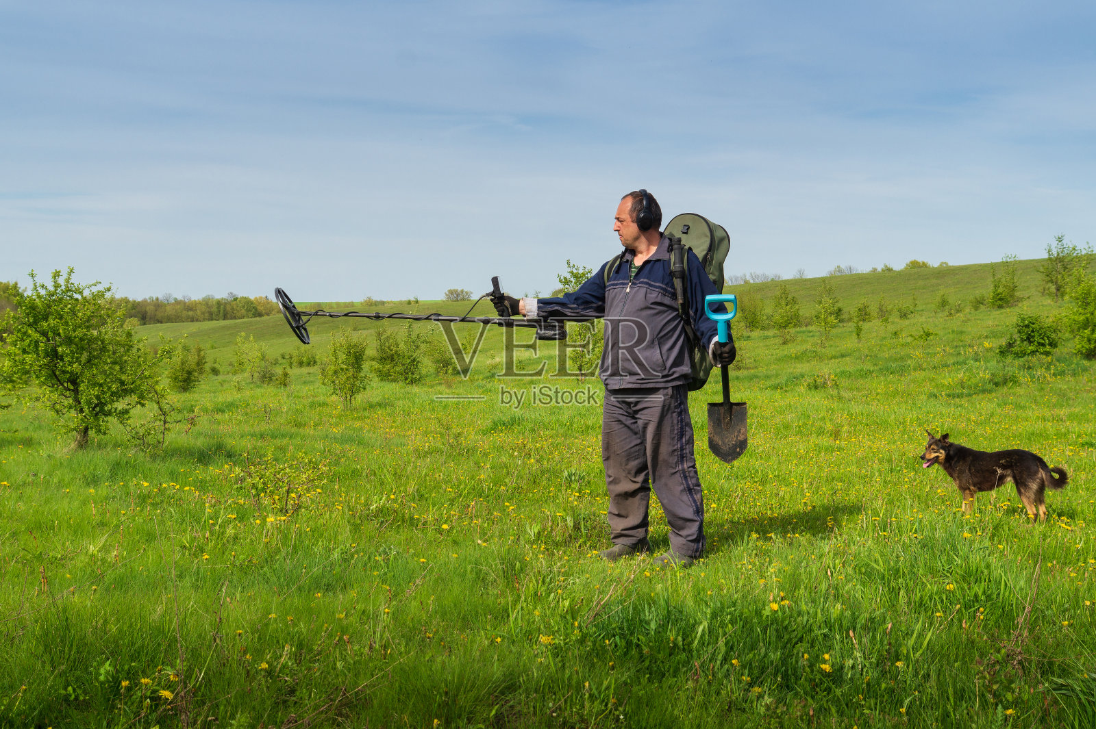 人和金属探测器。寻找地下金属的装置。在草坪上拿着铲子和探测器的建筑师。一名男子在寻找宝藏前调整了设备。照片摄影图片