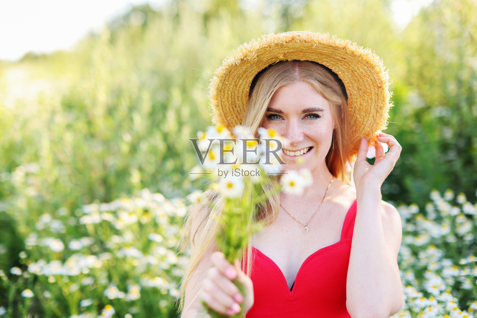 在背光下，一个女人在夕阳下的田野里穿着裙子，手里拿着一束雏菊照片摄影图片