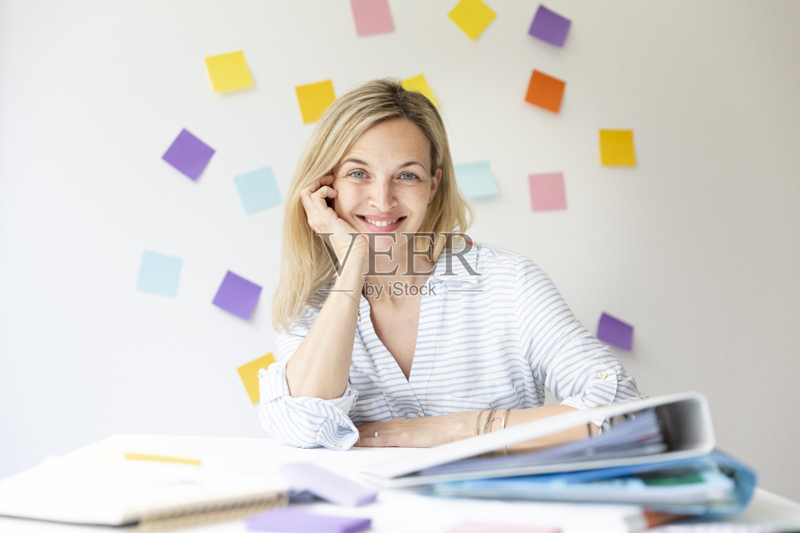 年轻漂亮的金发美女的肖像与美丽的笑声坐在前面的白色墙壁与彩色的便签照片摄影图片