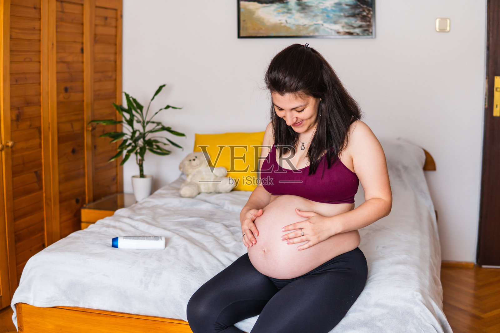 孕妇拥抱并爱抚着自己的腹部，并涂抹乳霜照片摄影图片