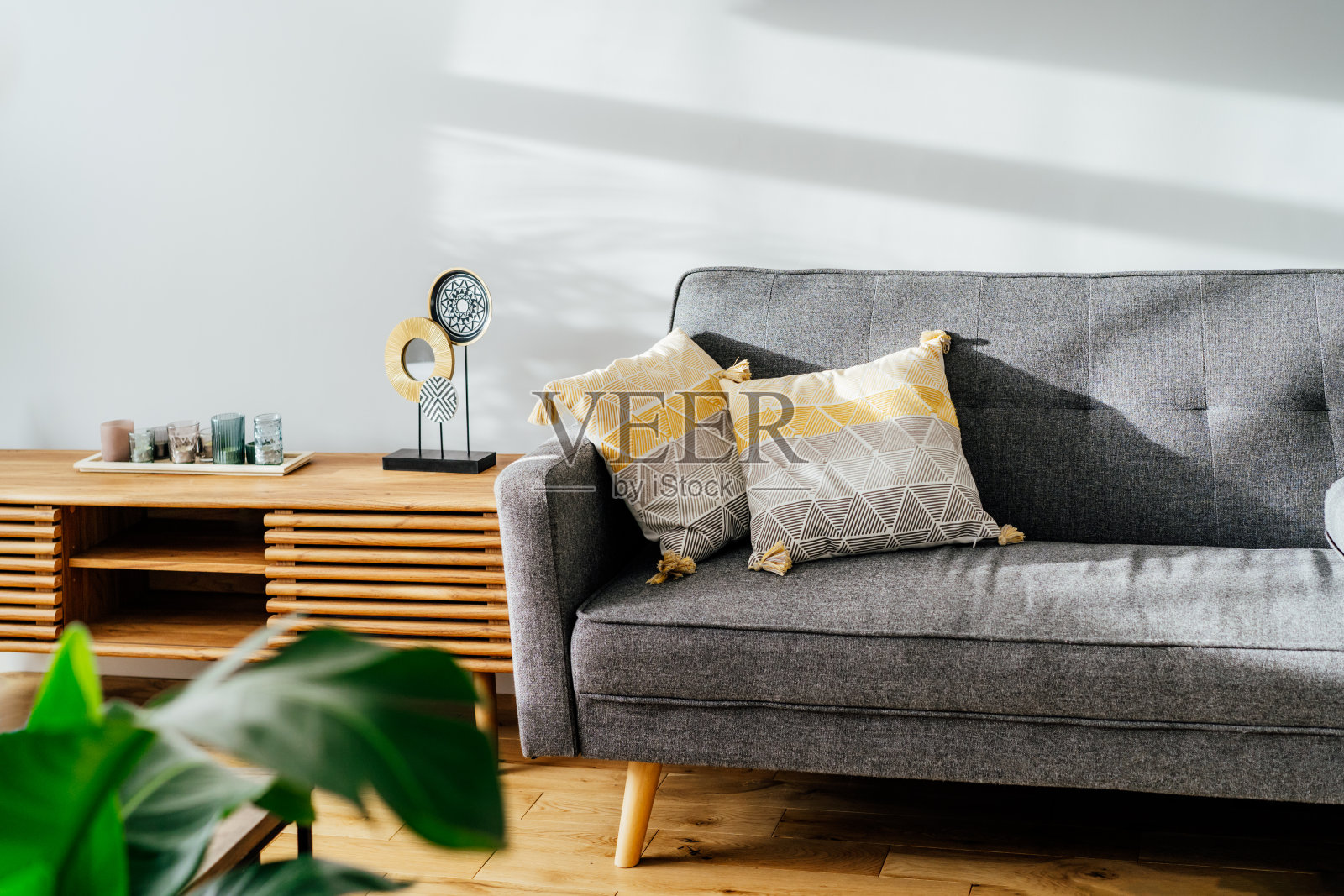 时尚的客厅室内与设计师控制台decor和灰色沙发与图形枕头。白色的墙壁，绿色的花盆。轻质橡木拼花地板。现代斯堪的纳维亚风格的室内设计。照片摄影图片