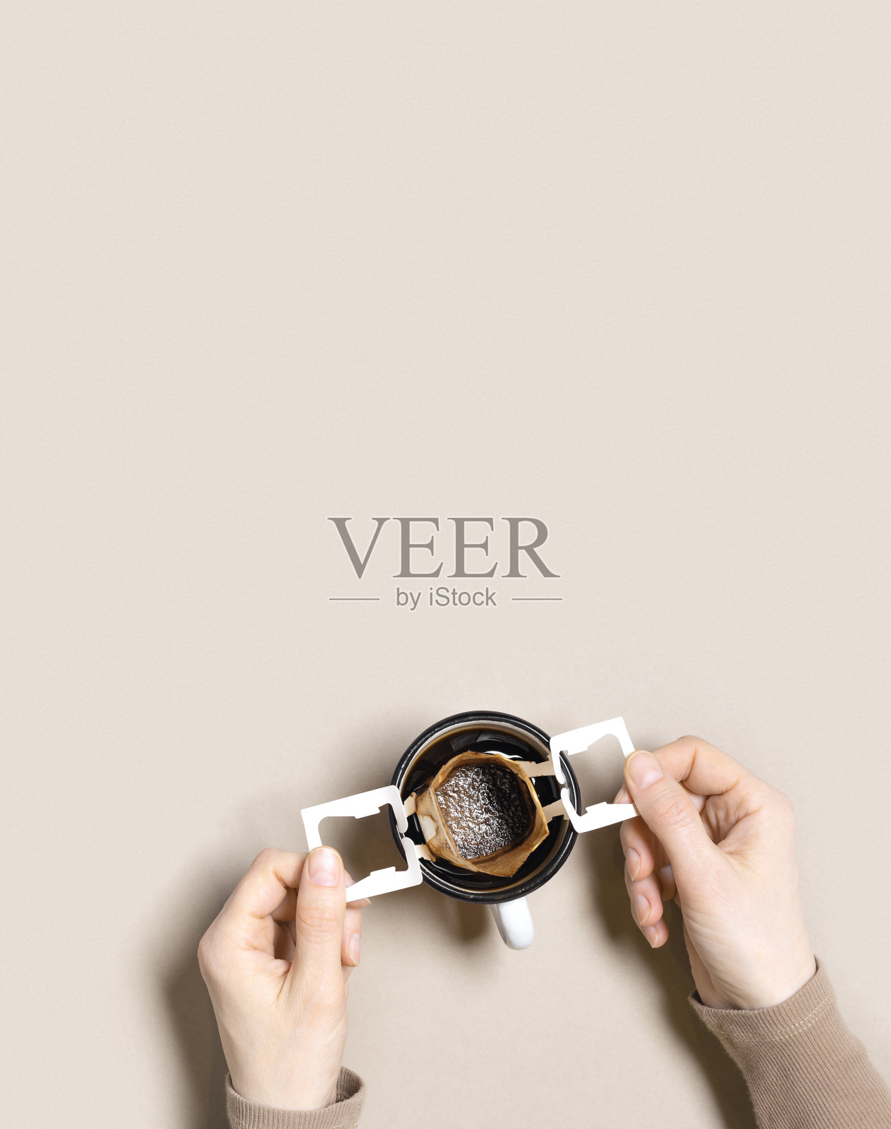 女人手握杯子，在杯子里做黑咖啡喝，咖啡袋滴咖啡磨在杯子里煮，纸袋滴咖啡过滤器，米色背景，俯视图，最小的平面布局照片摄影图片