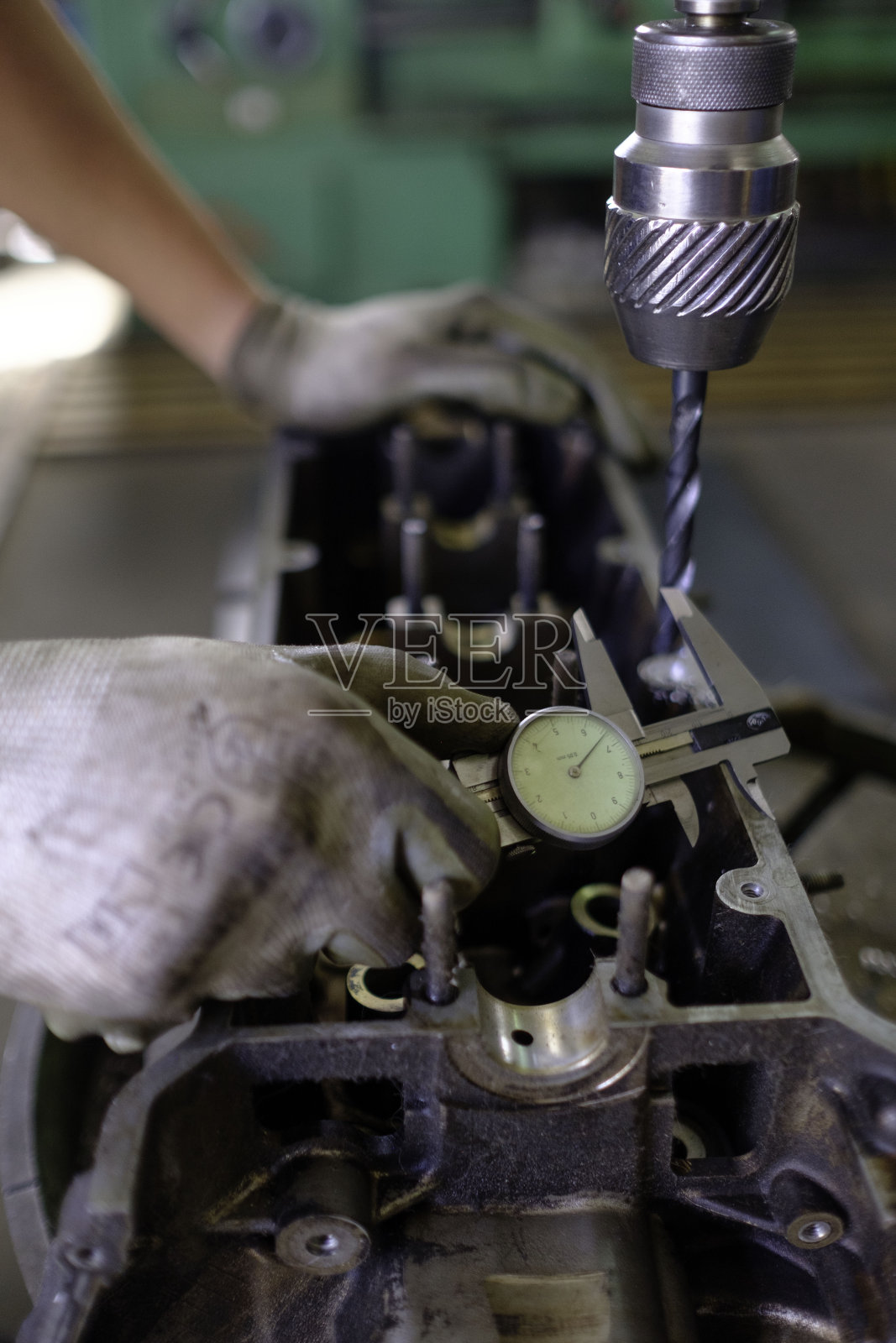 家庭车间里戴着手套用垂直钻工作的白人技术员。照片摄影图片